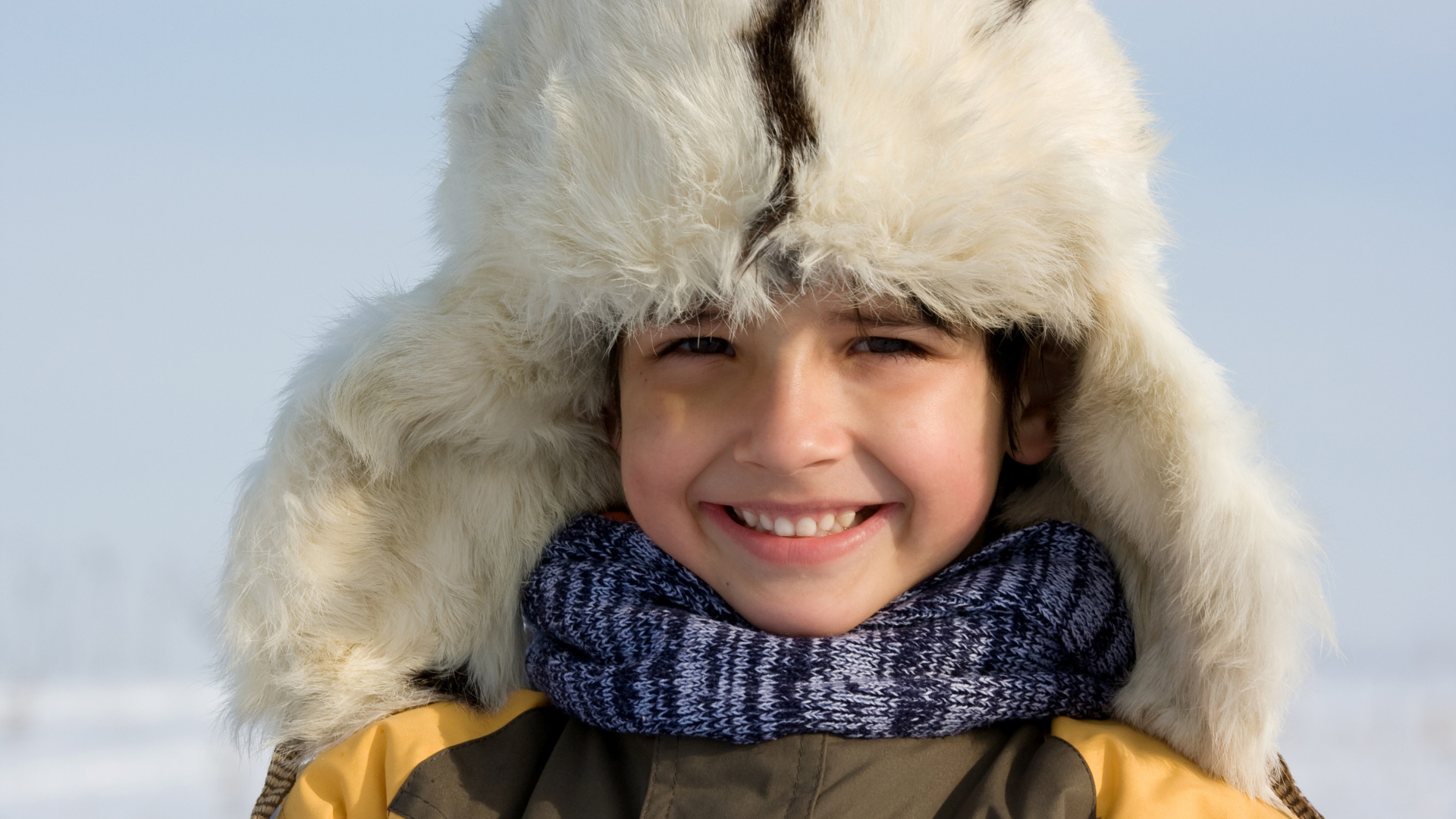 Маленький улыбающийся мальчик в теплой шапке зимой