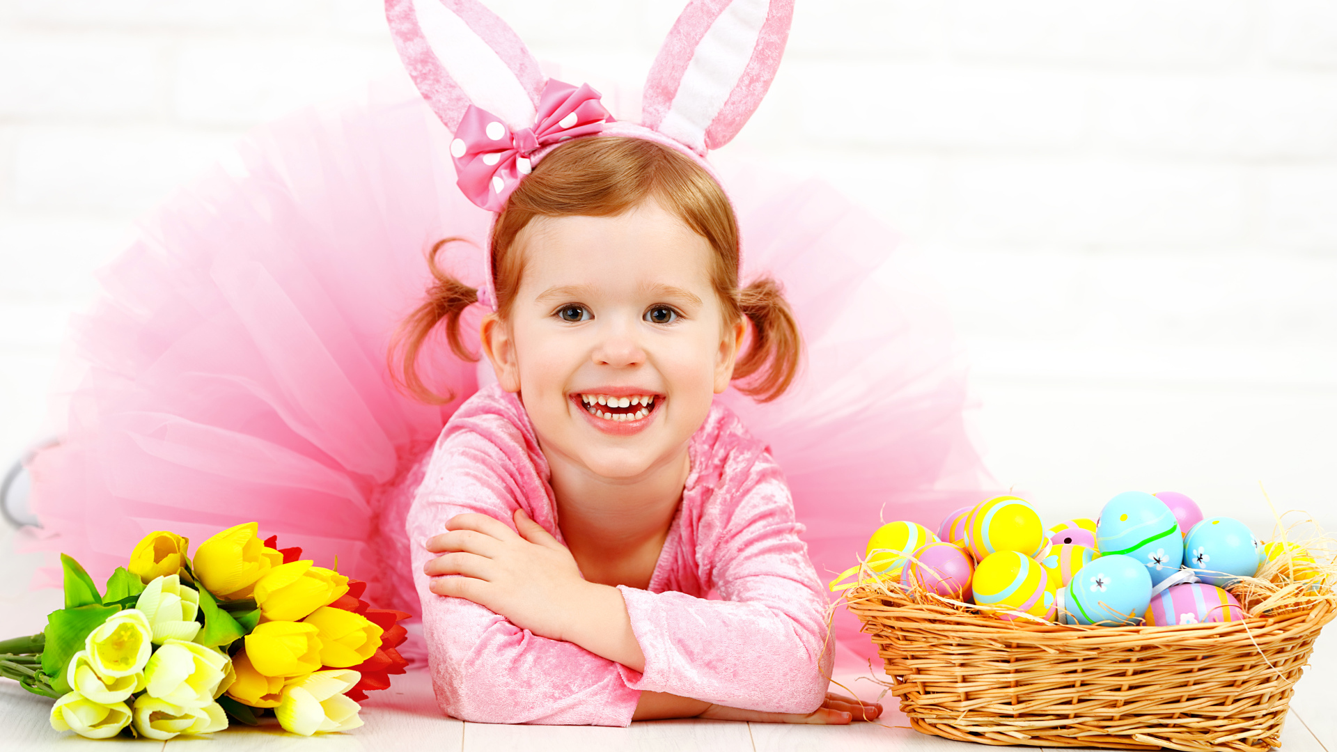 Маленькая улыбающаяся девочка в розовом с пасхальными яйцами и букетом тюльпанов