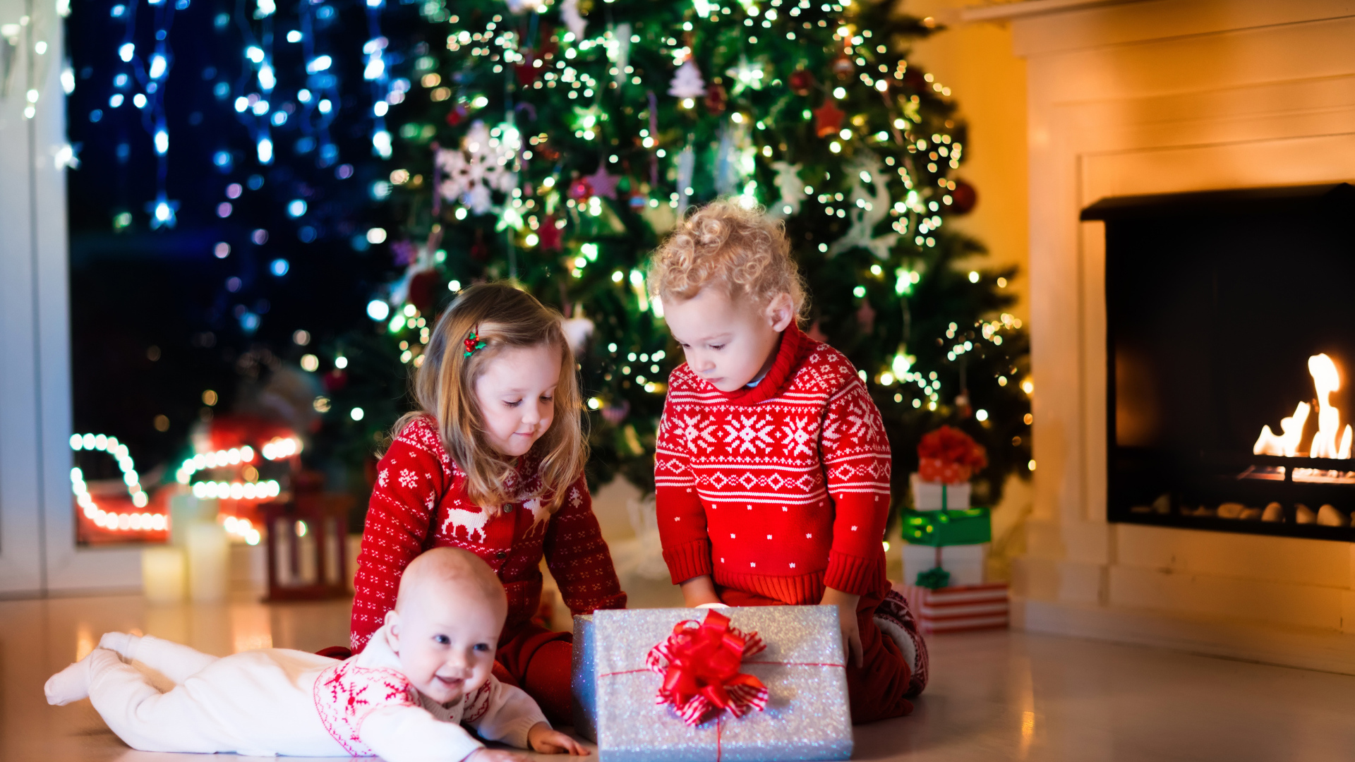 Маленькие дети с новогодним подарком у наряженной елки