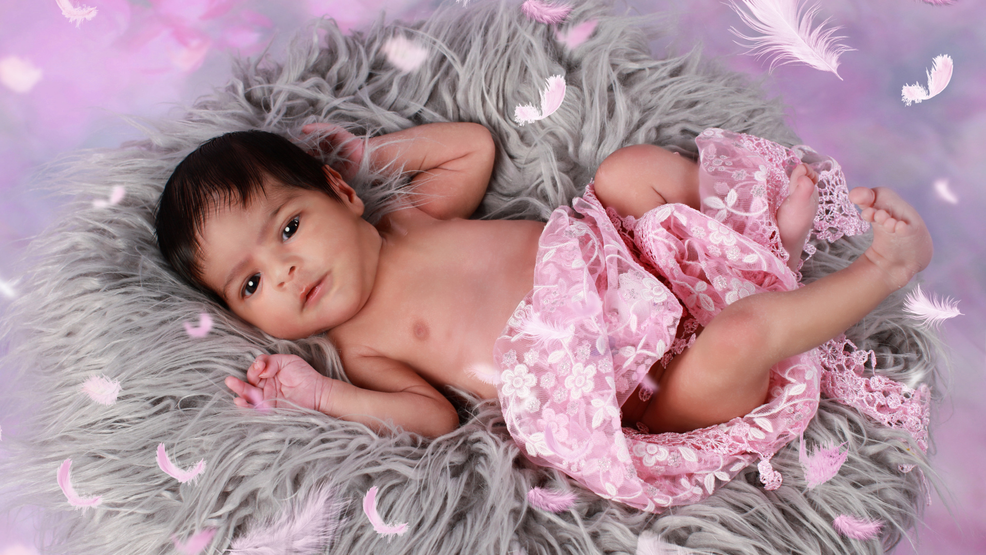 Младенец лежит на сером меховом покрывале 