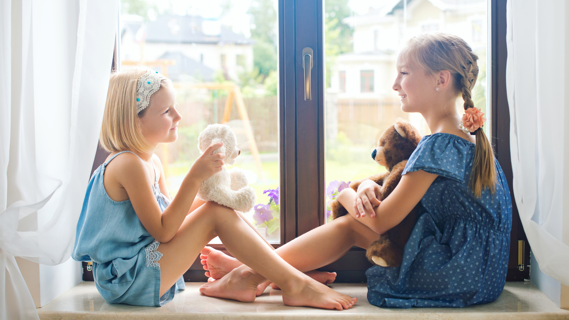 Две маленькие девочки с игрушками сидят на подоконнике у окна