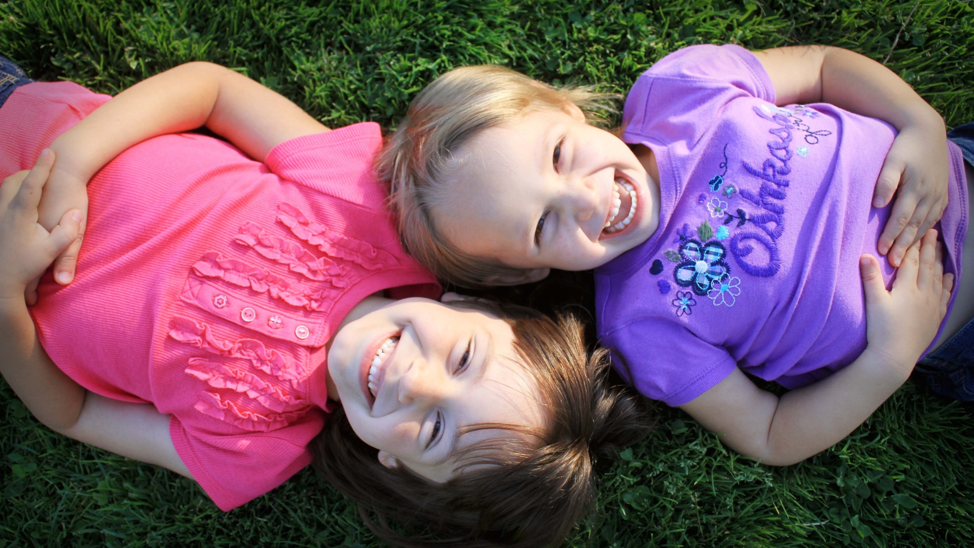 Две маленьких улыбающихся девочки лежат на зеленой траве