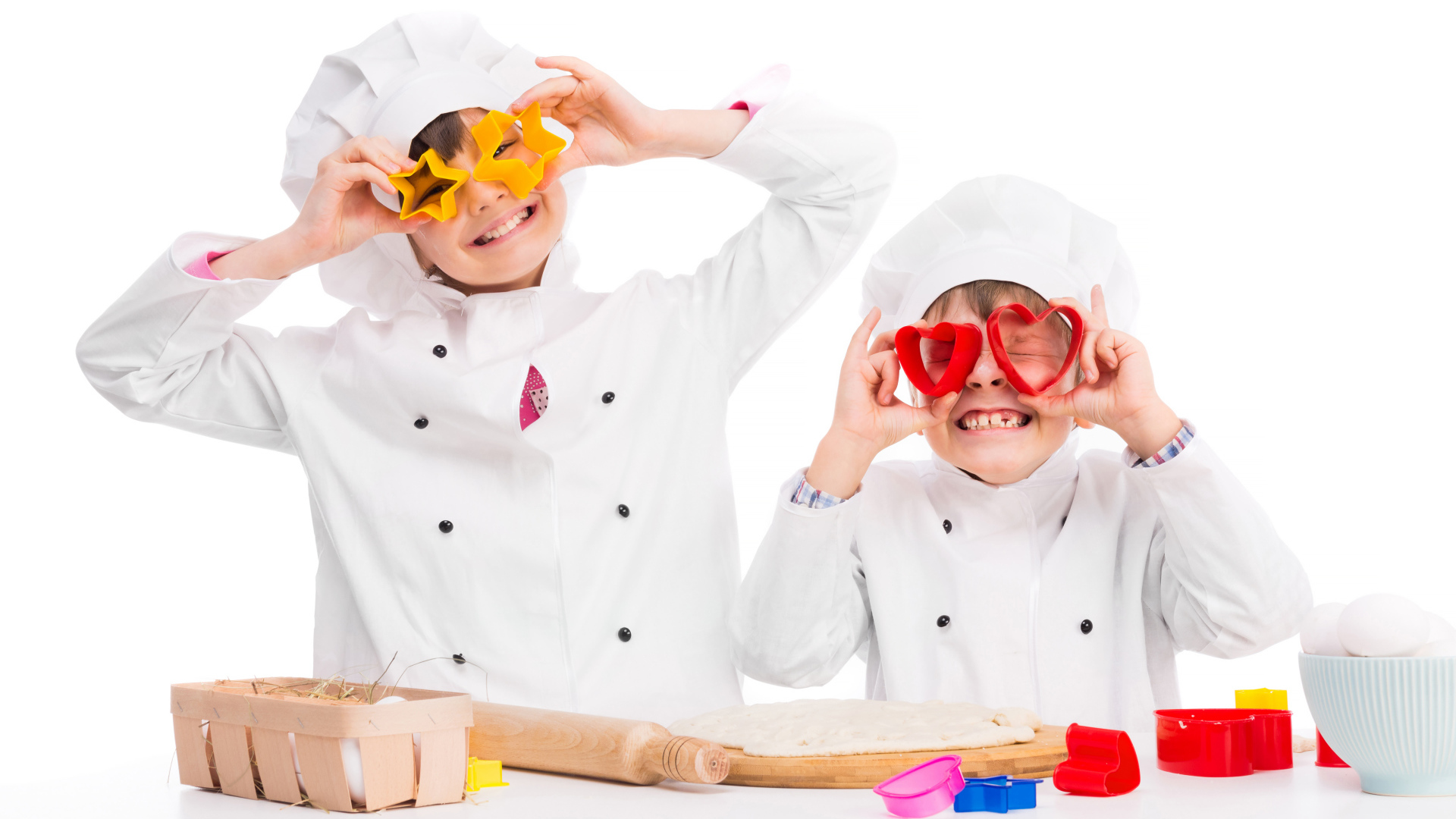 Два маленьких ребенка в костюмах повара готовят на кухне печенье