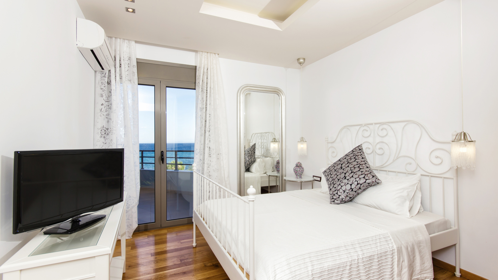 Светлая спальня с большой белой кроватью и телевизором 