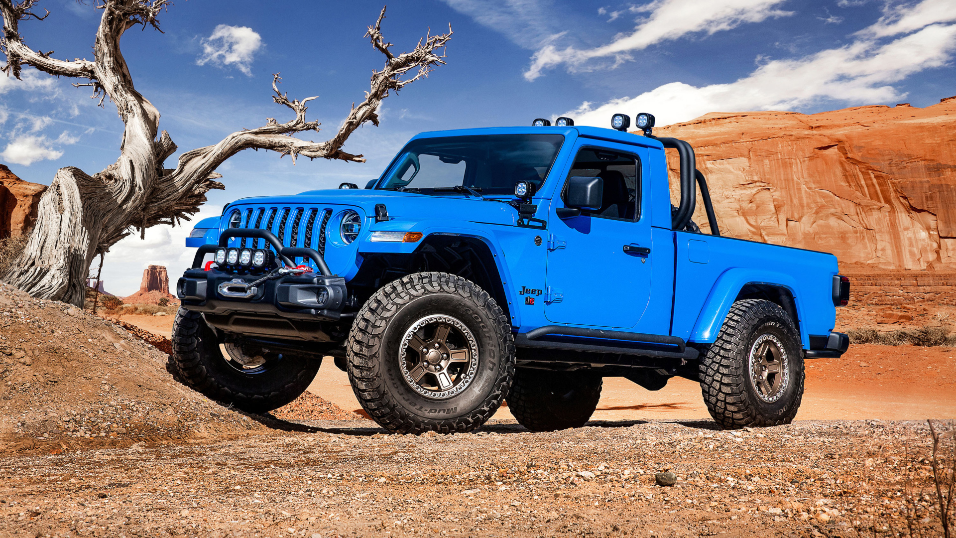 Синий пикап Jeep J6, 2019 года на фоне гор у сухого дерева