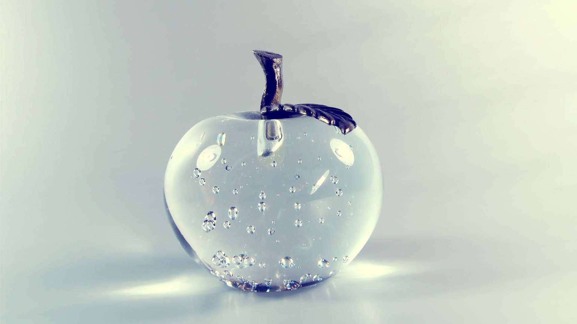 Стеклянное яблоко на сером фоне 