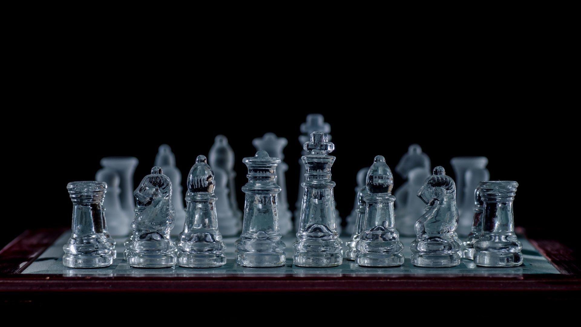 Стеклянные шахматы на доске на черном фоне