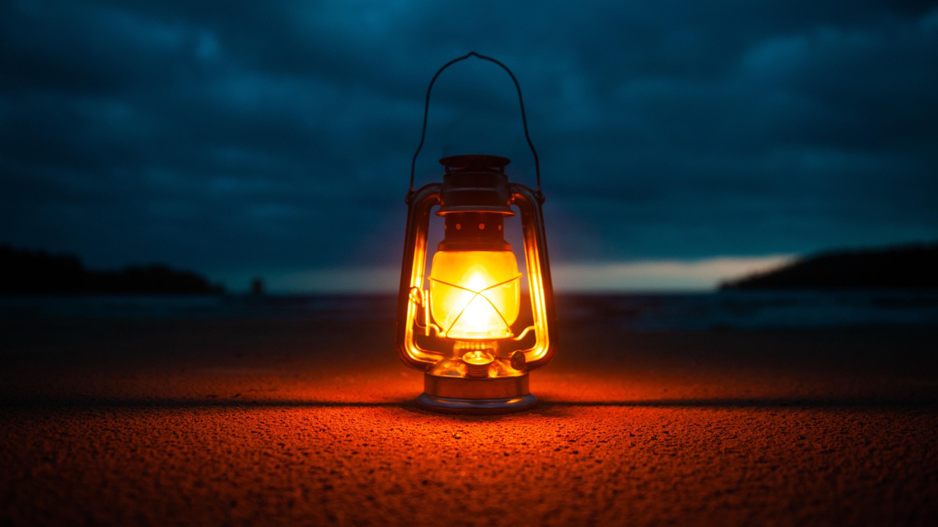 Включенный фонарь стоит на песке у моря 