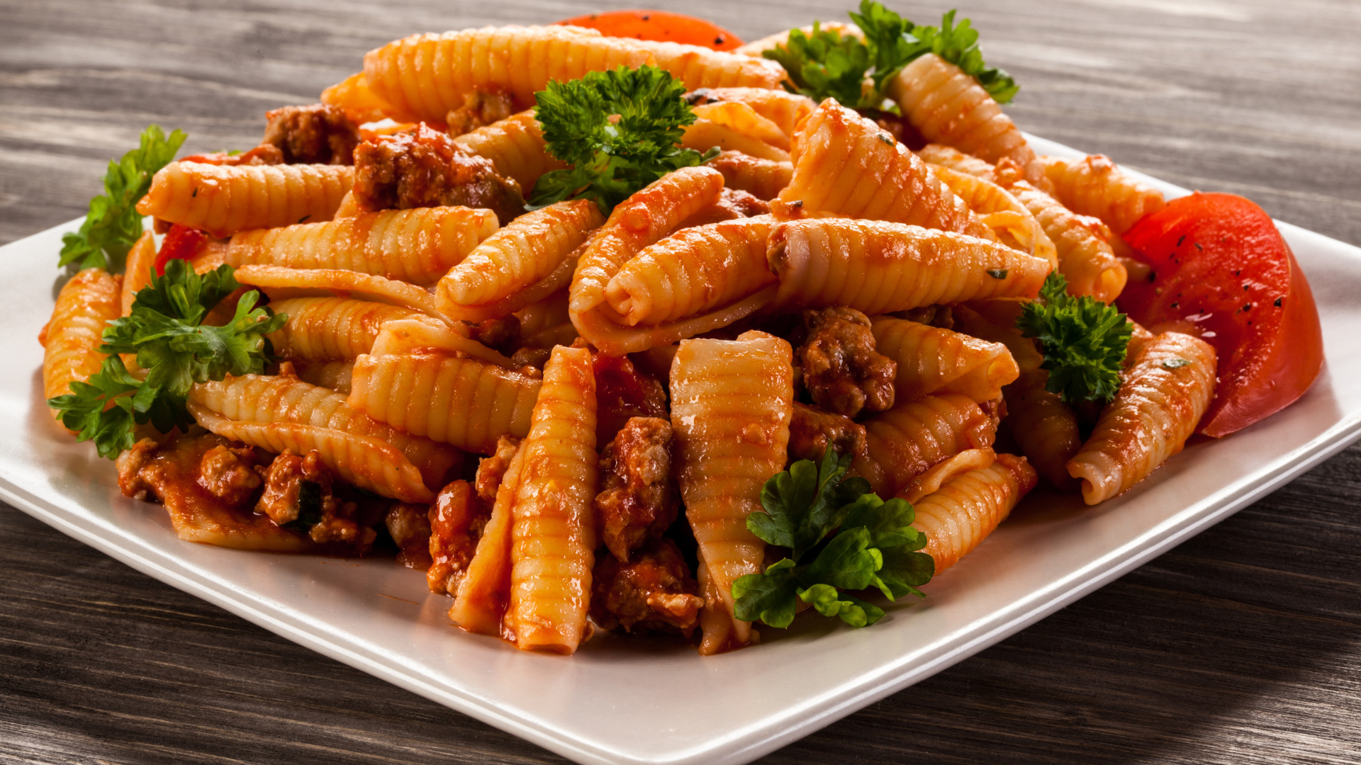 Паста с мясом, петрушкой и помидорами на белой тарелке