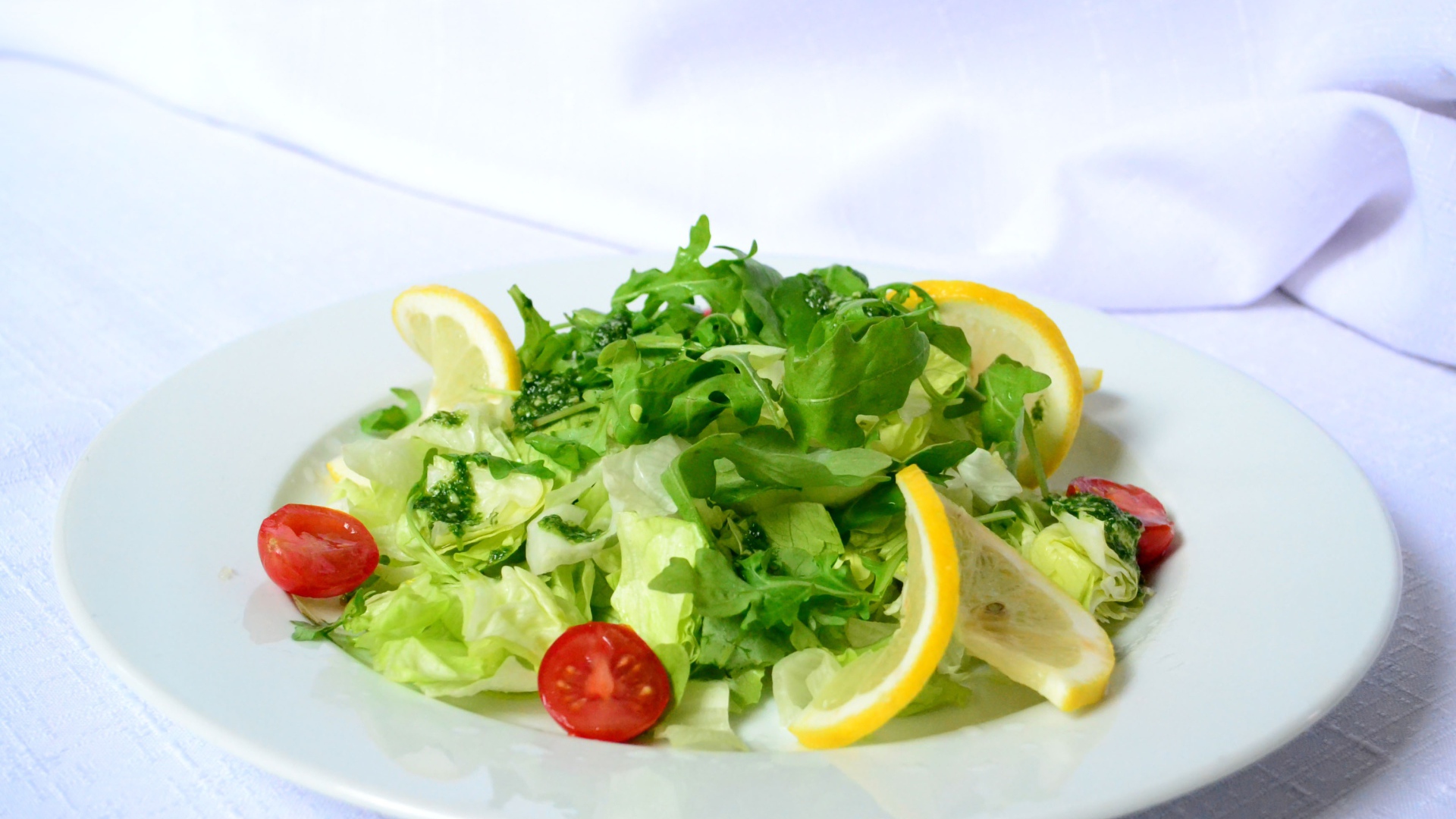 Салат с рукколой, лимоном и помидорами на белой тарелке