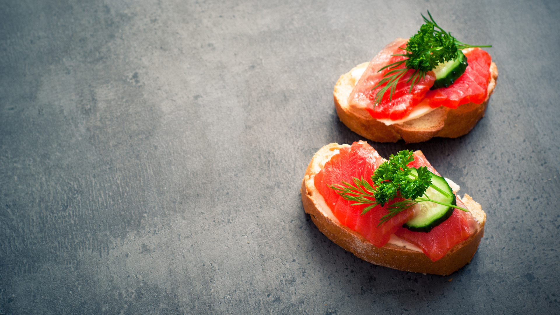 Два бутерброда с красной рыбой, огурцом и зеленью на черном фоне
