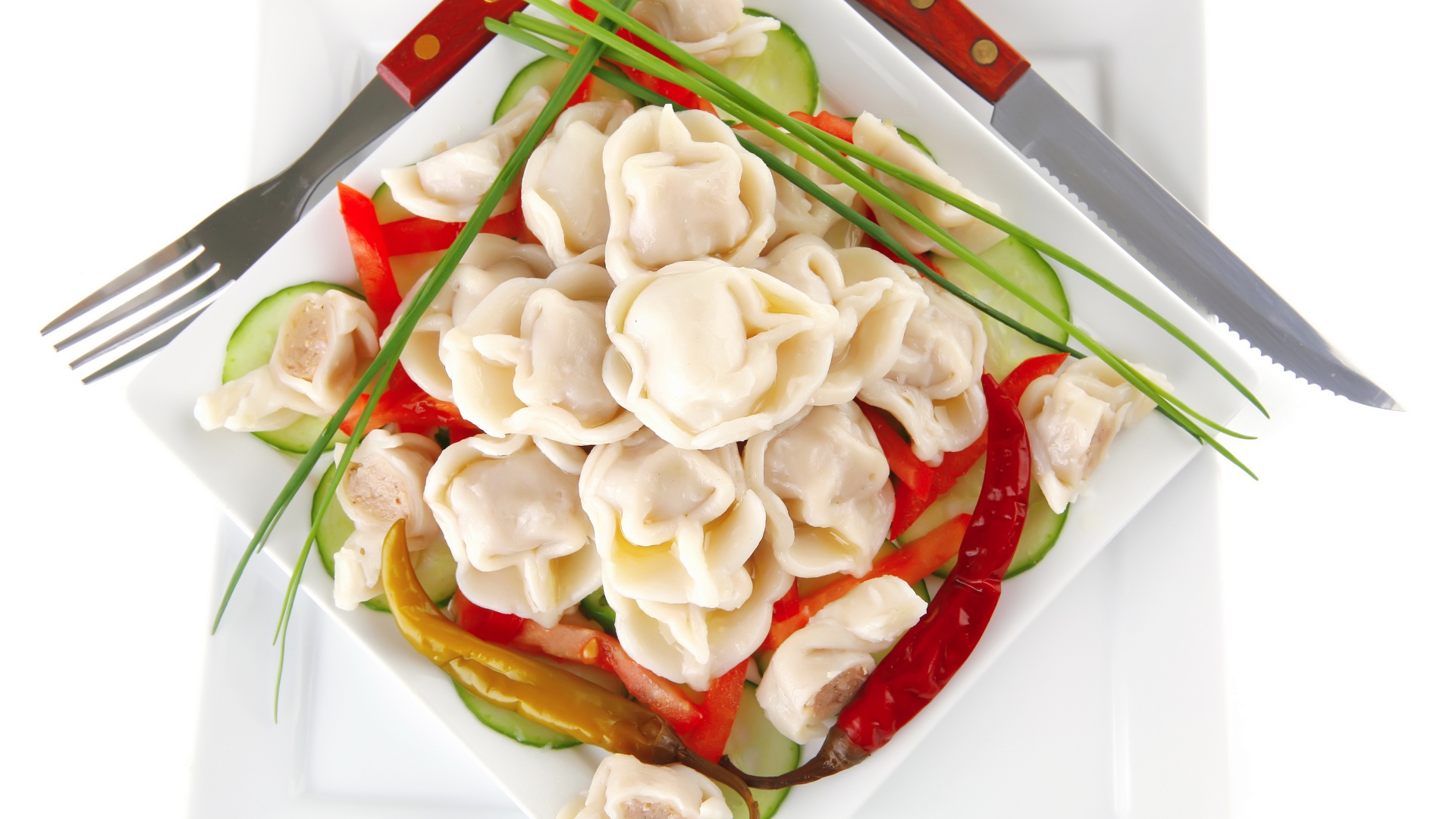 Белая тарелка с пельменями, красным перцем и огурцами