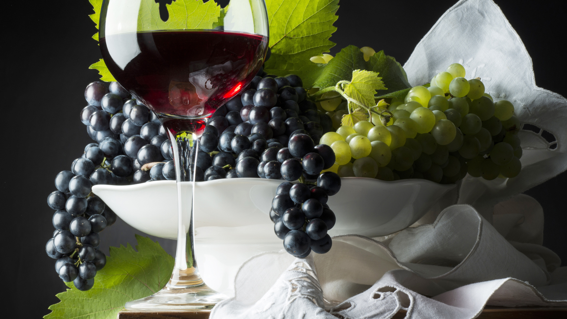 Бокал красного вина на столе с белым и синим виноградом