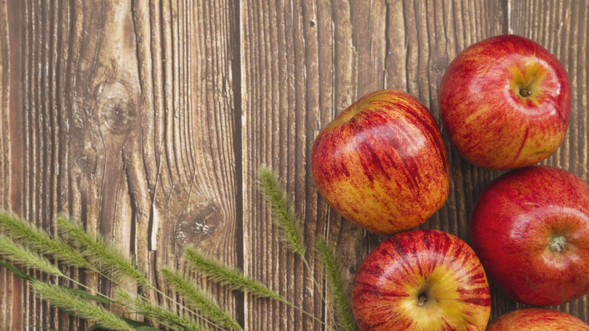 Красные яблоки на деревянном фоне с зелеными колосками