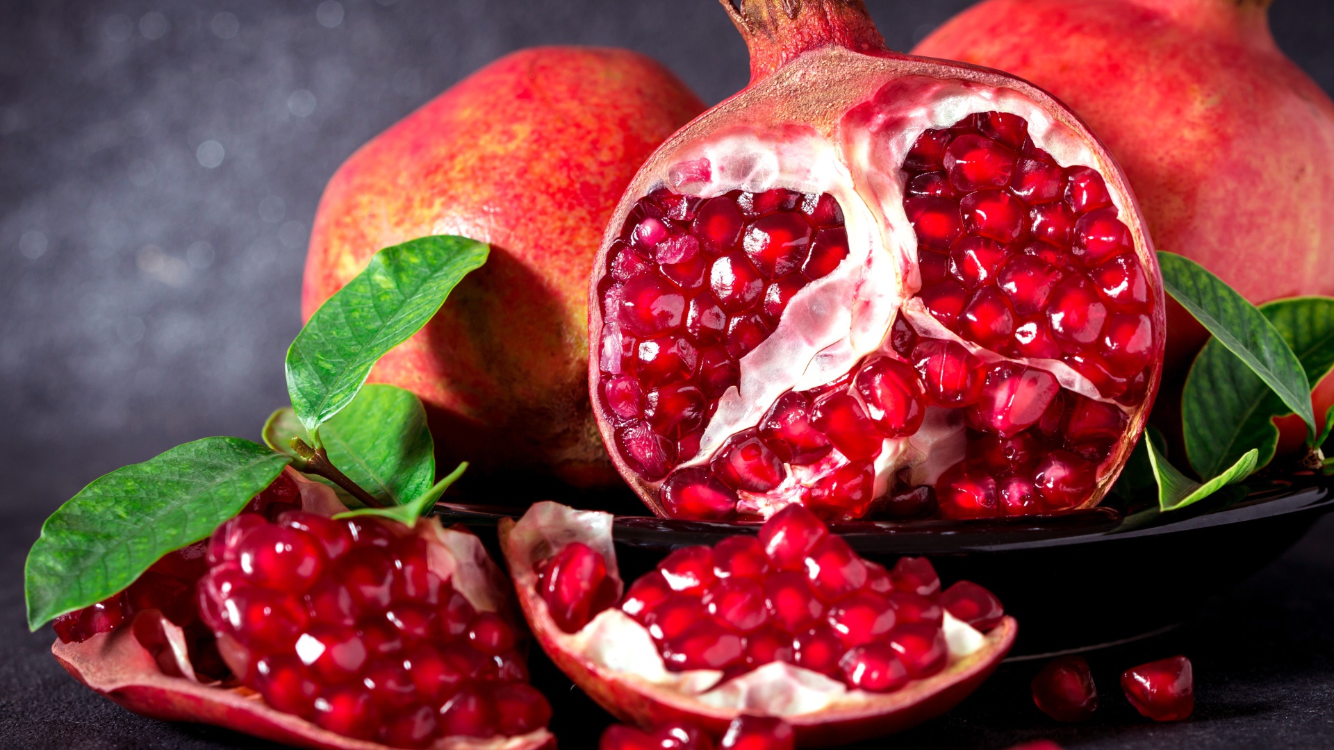 Красные гранаты с зернами и зелеными листьями на сером фоне