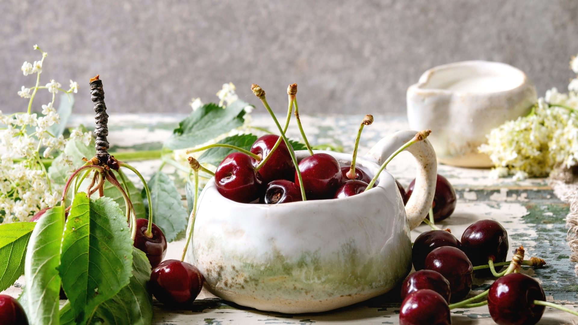 Спелые красные черешни на столе в белом чайнике