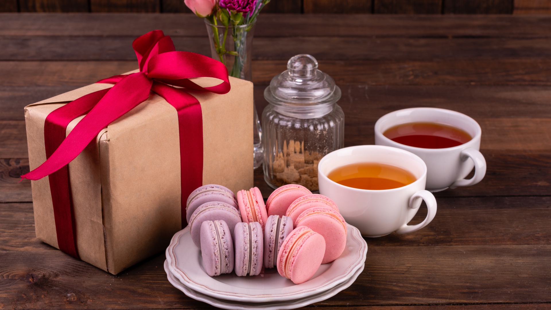Подарок с красной лентой на столе с макарунами и чаем 