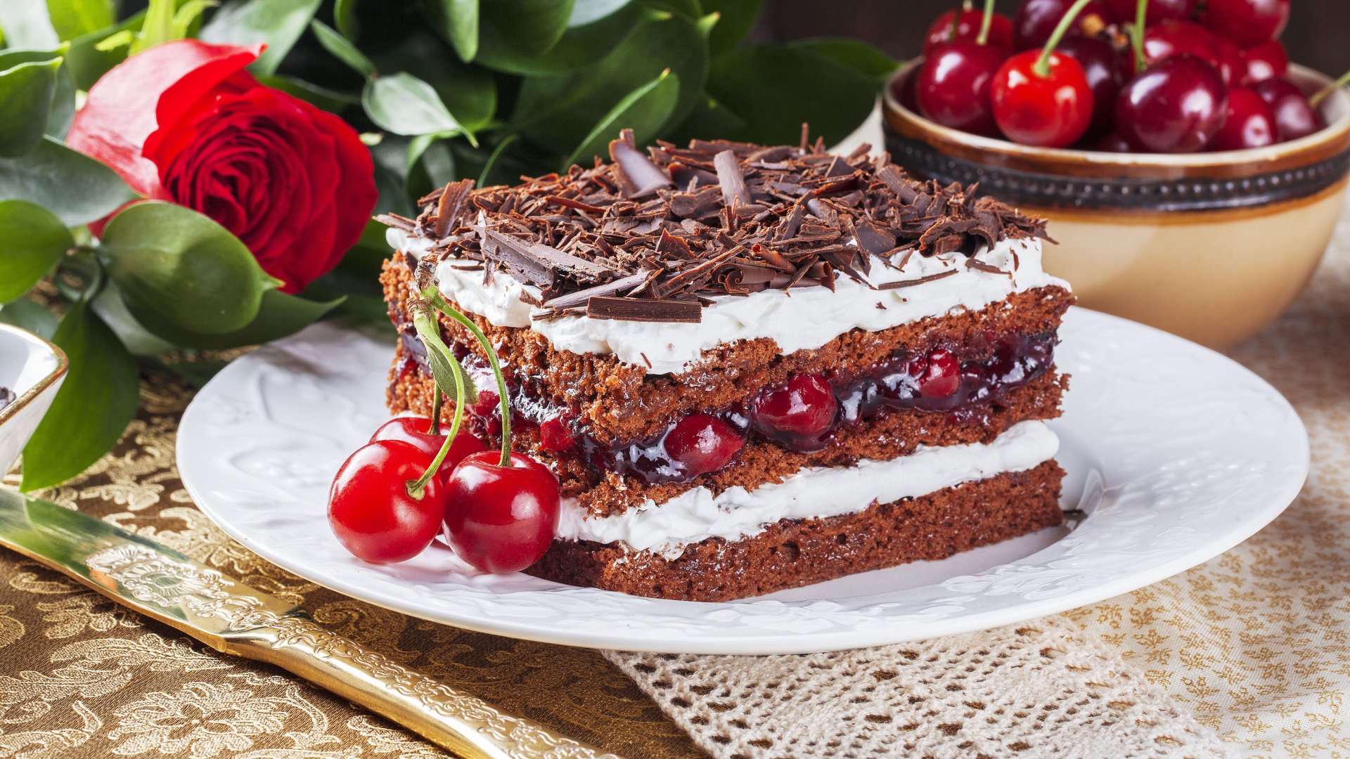 Кусок торта с вишней, шоколадной крошкой на столе с розой