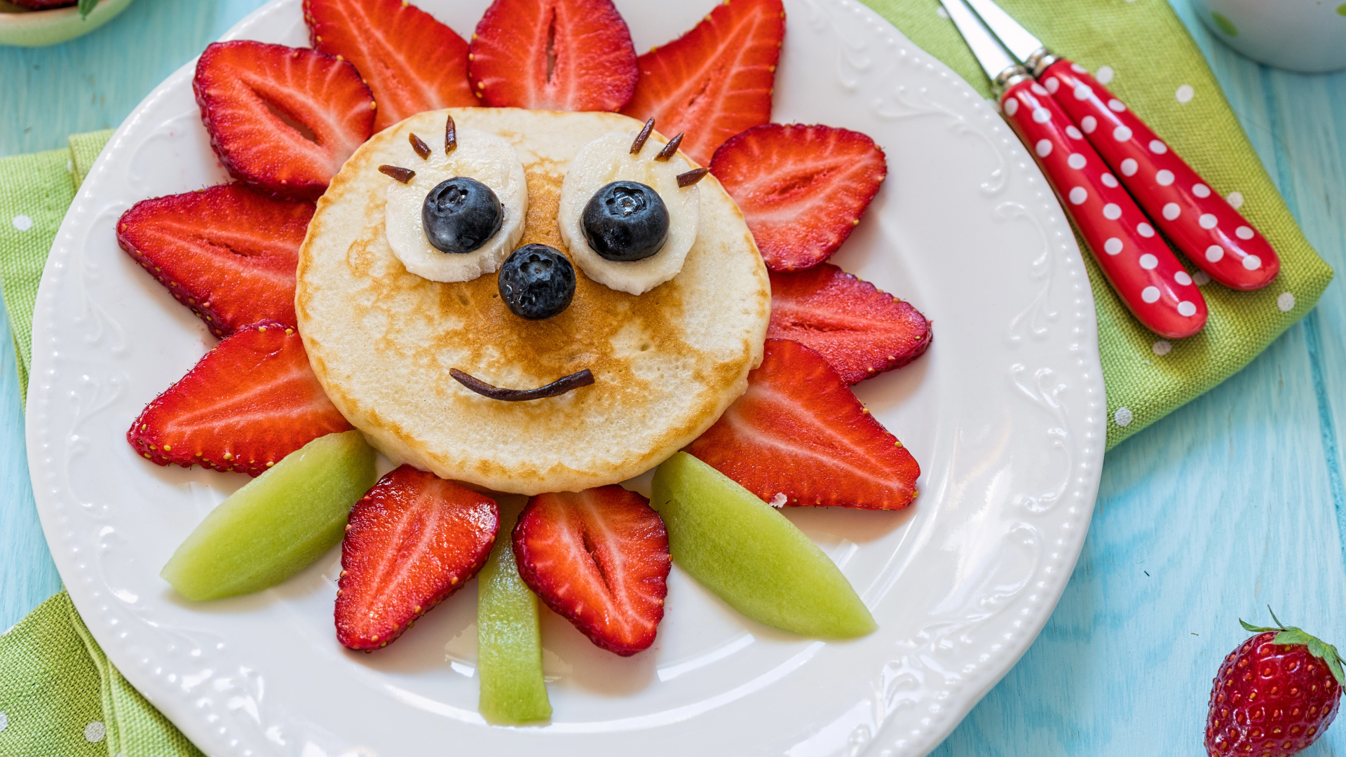 Цветок из клубники, оладьей и киви  на белой тарелке