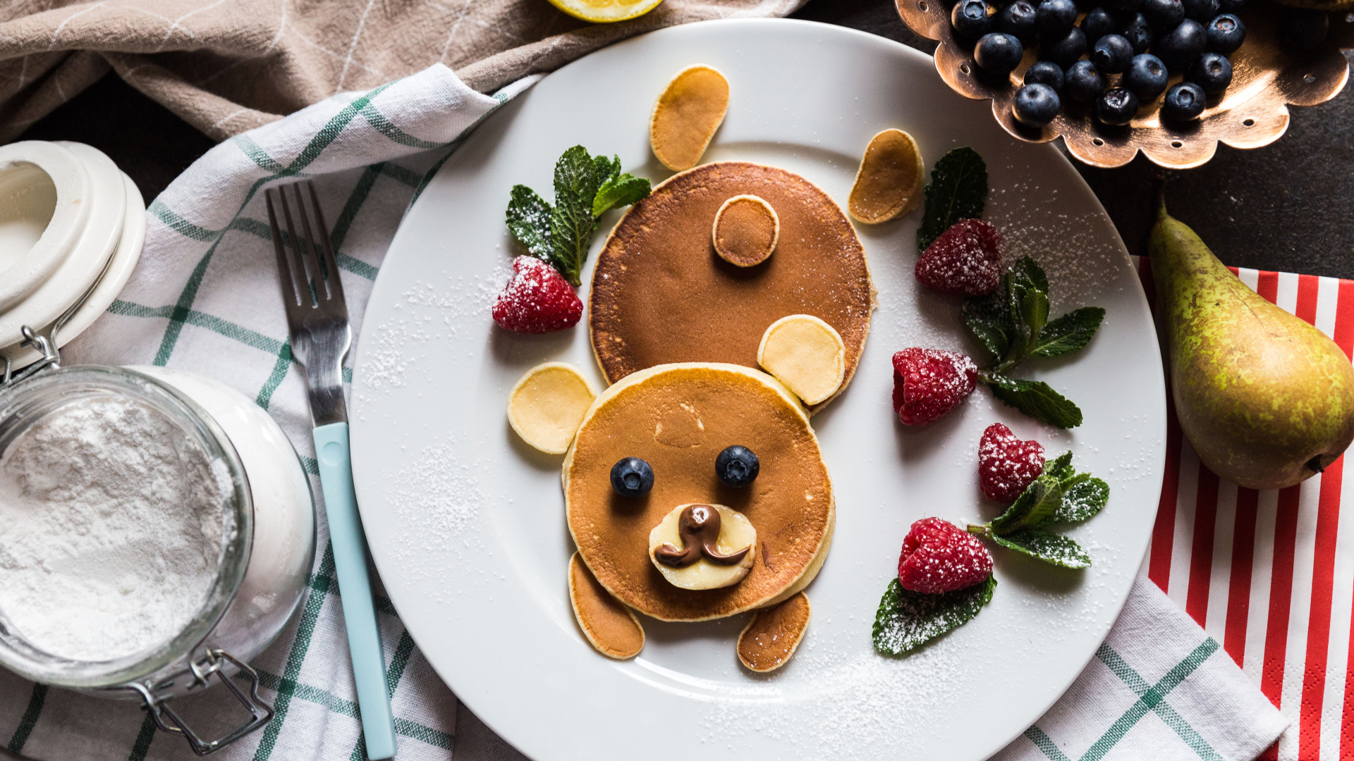 Медведь из оладьев на тарелке с малиной и сахарной пудрой