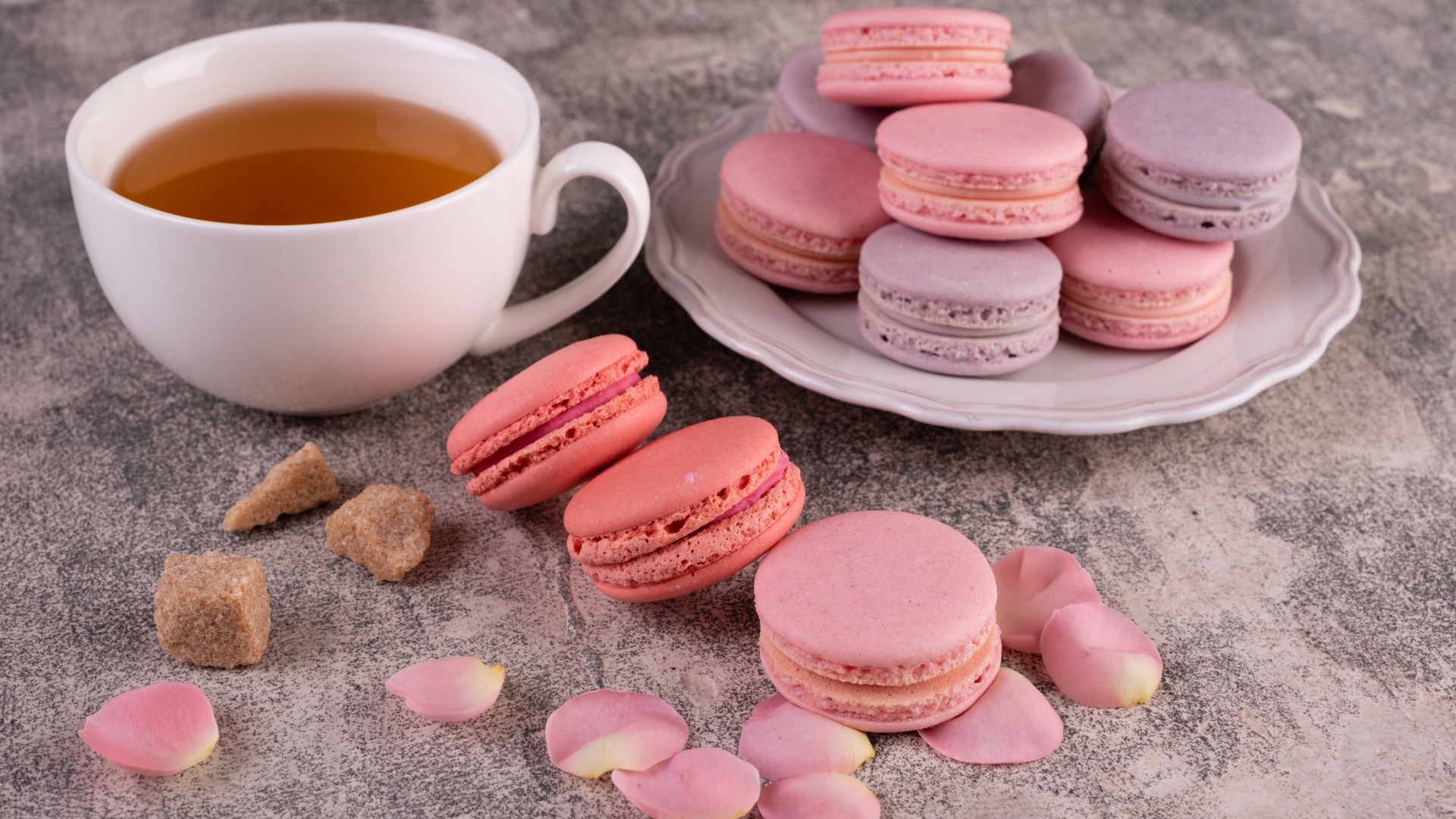 Сладкий десерт макарун на столе с чашкой чая, сахаром и лепестками розы