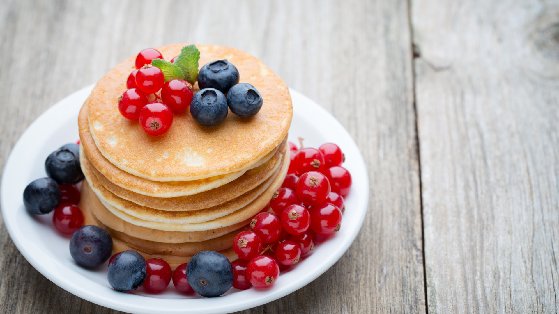 Вкусные оладьи на тарелке с ягодами красной смородины и черники