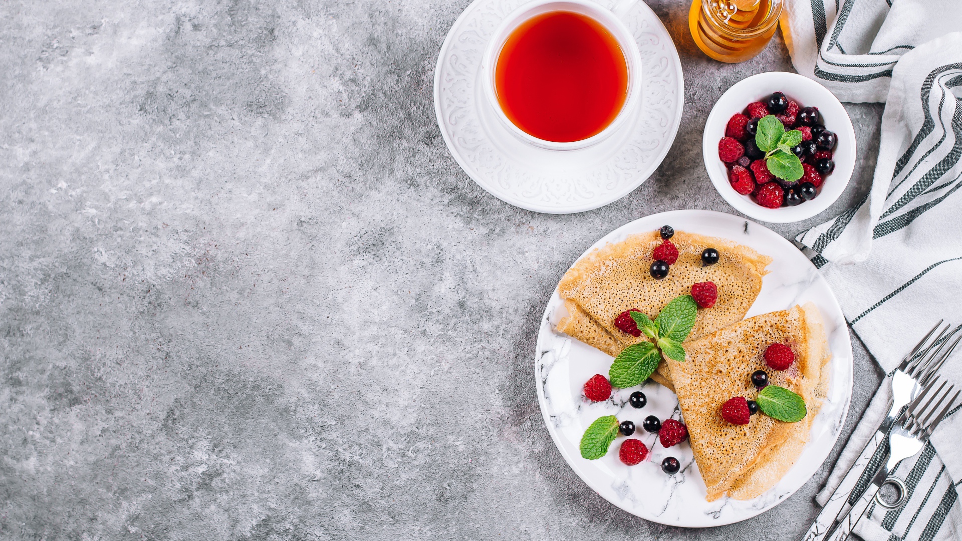 Тонкие блинчики на столе с ягодами, чаем и медом