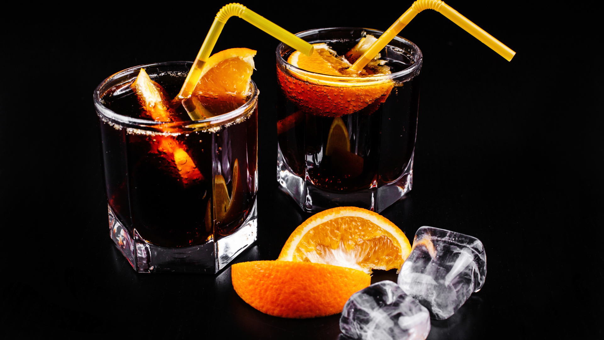 Коктейль с кусочками апельсина на черном фоне со льдом