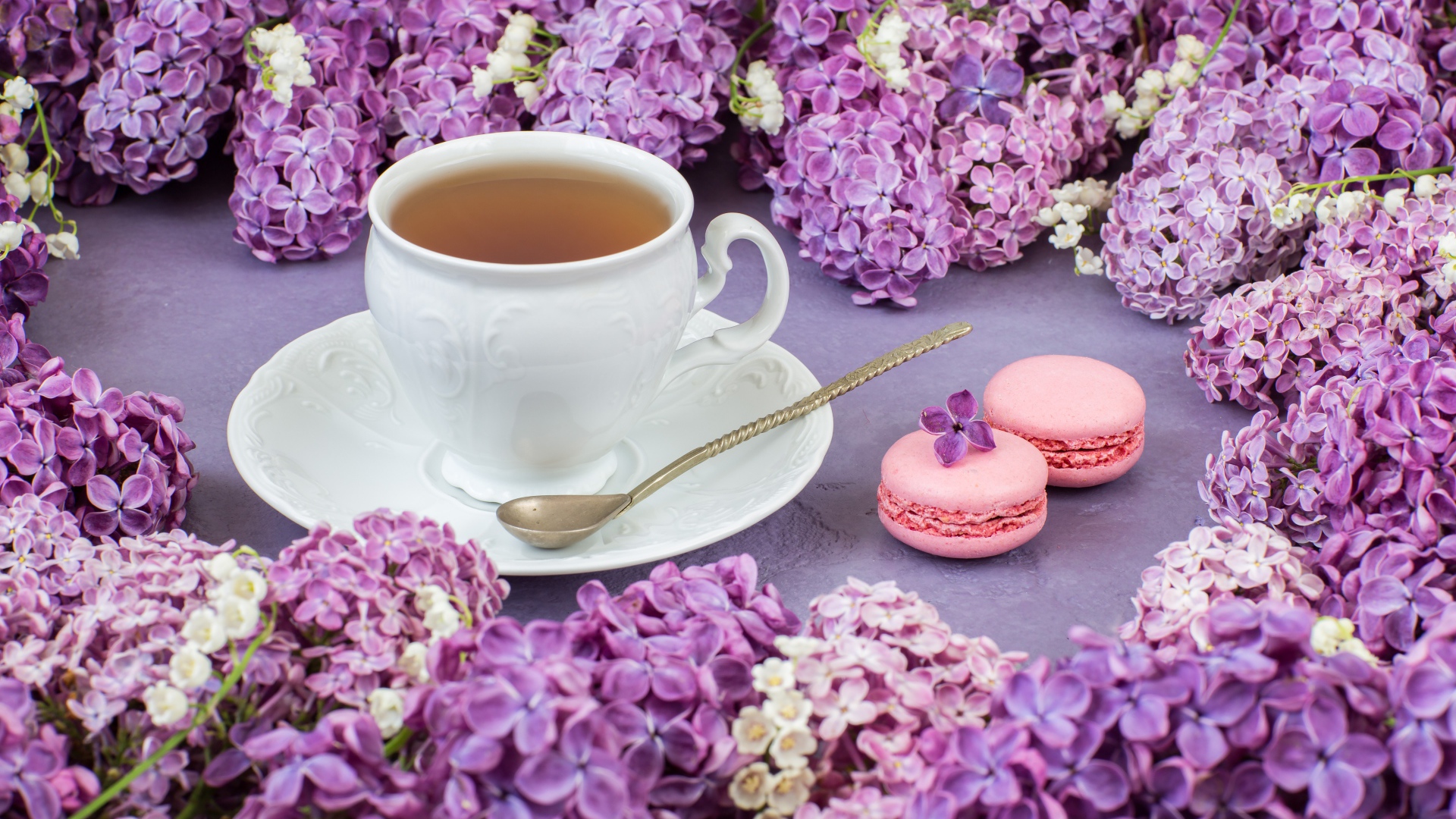Чашка чая на столе с цветами сирени и десертом макарон