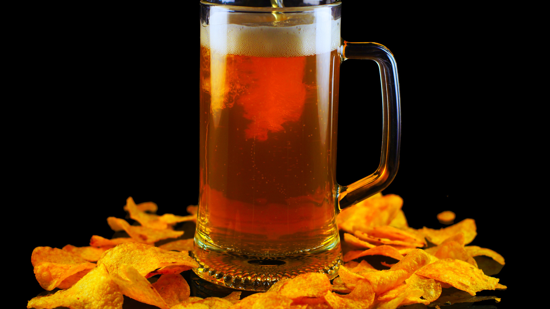 Бокал пива с чипсами на черном фоне