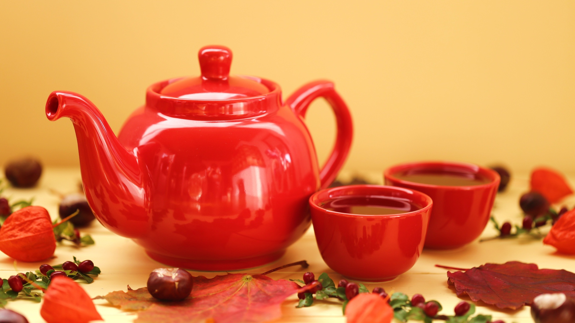 Красный чайник с чашками на столе осенью 