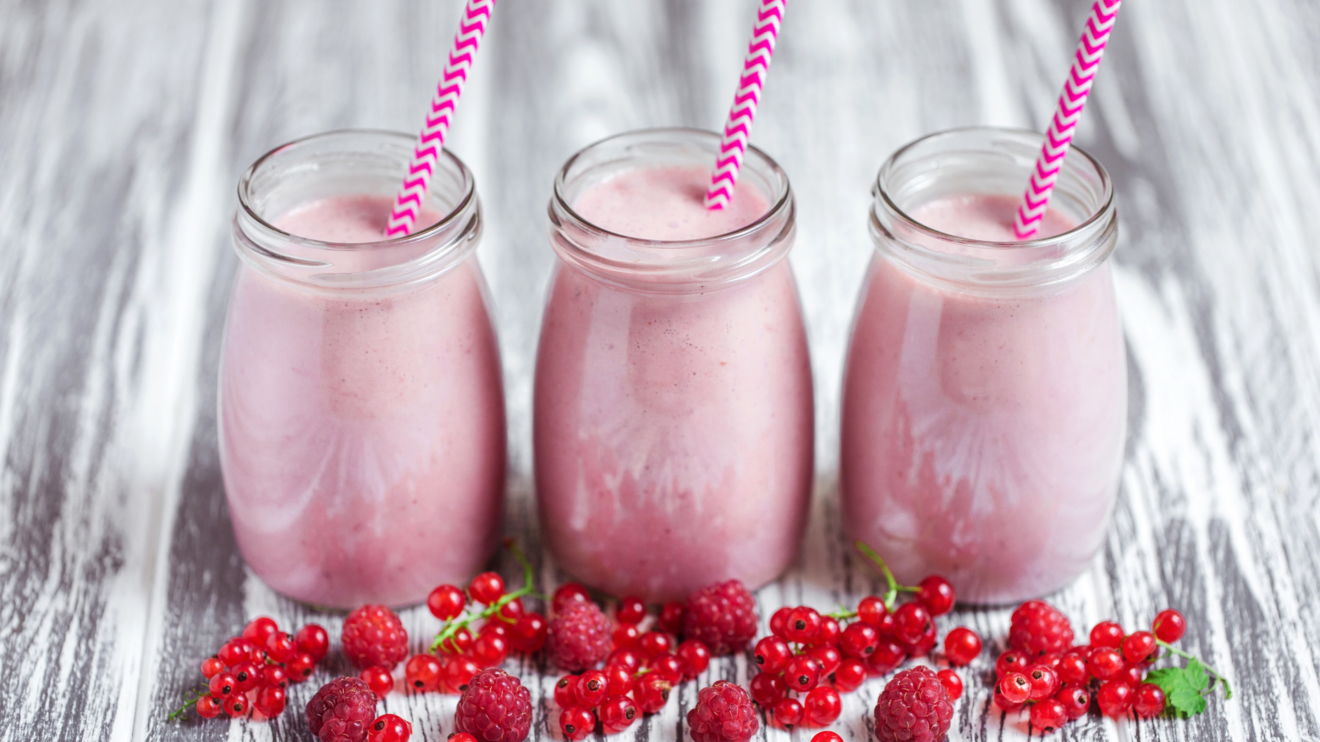 Три банки ягодного  смузи на столе с ягодами малины и смородины