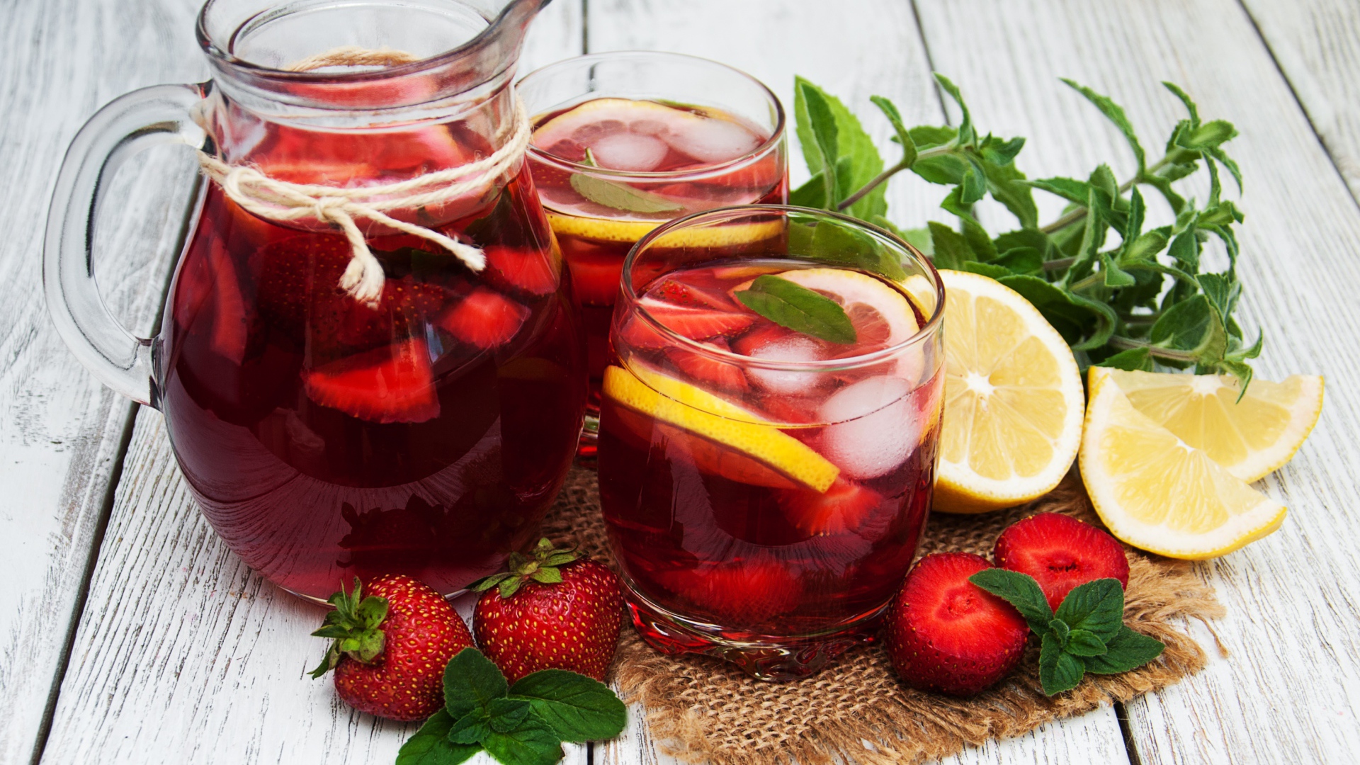 Два стакана мохито на столе с графином, лимоном, клубникой и мятой