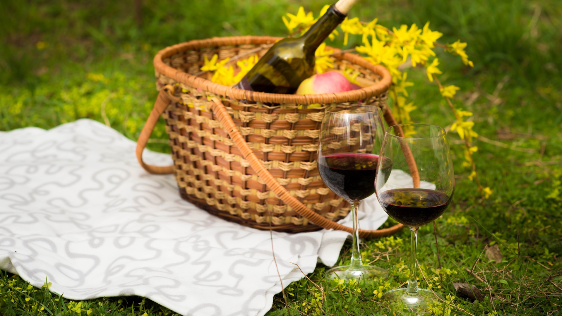 Два бокала вина с корзиной на зеленой траве для пикника 
