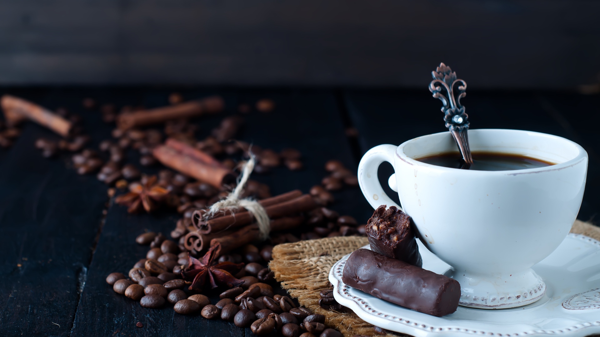 Белая чашка кофе на столе с конфетами, корицей, бадьяном и зернами