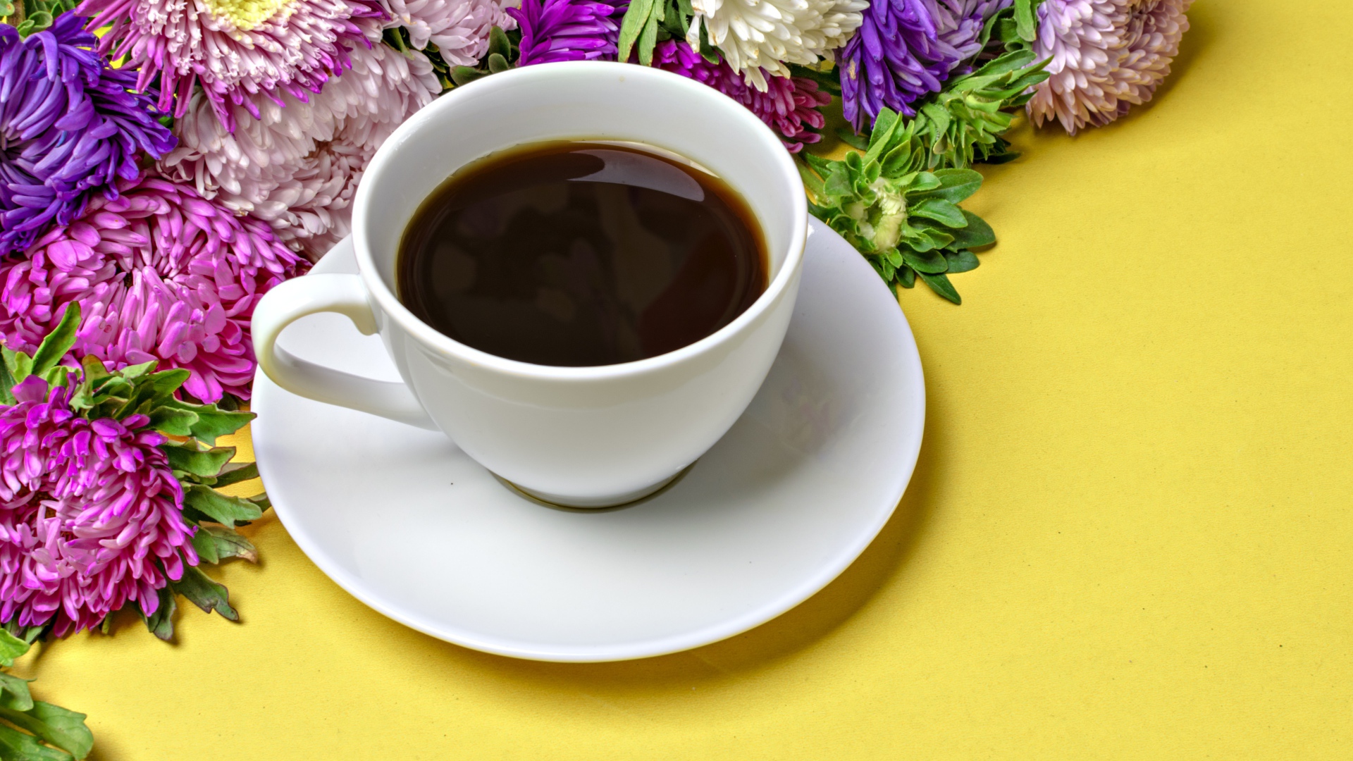 Белая чашка кофе на желтом фоне с букетом цветов астры