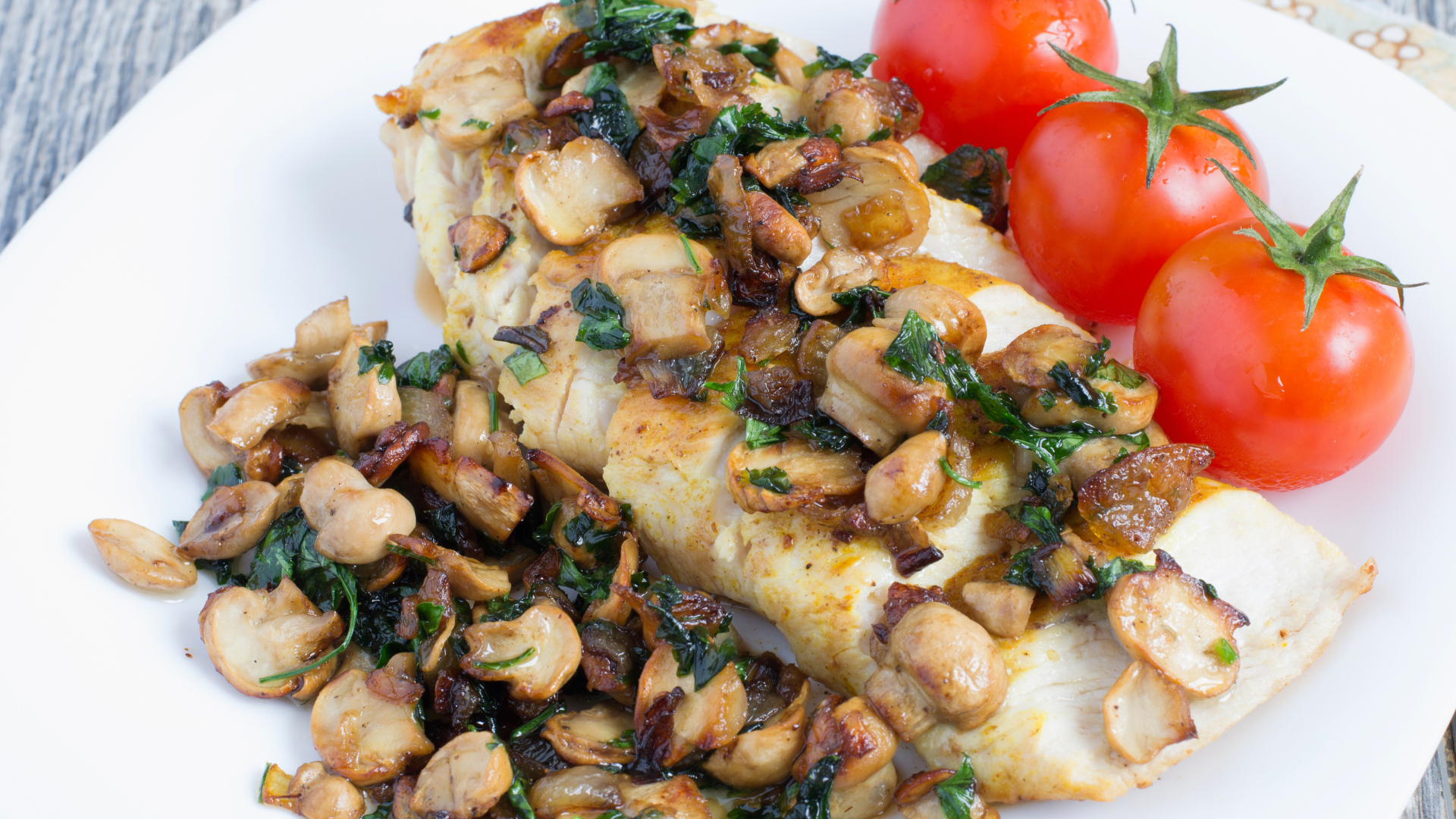 Аппетитный кусок куриного филе с грибами на тарелке с помидорами 