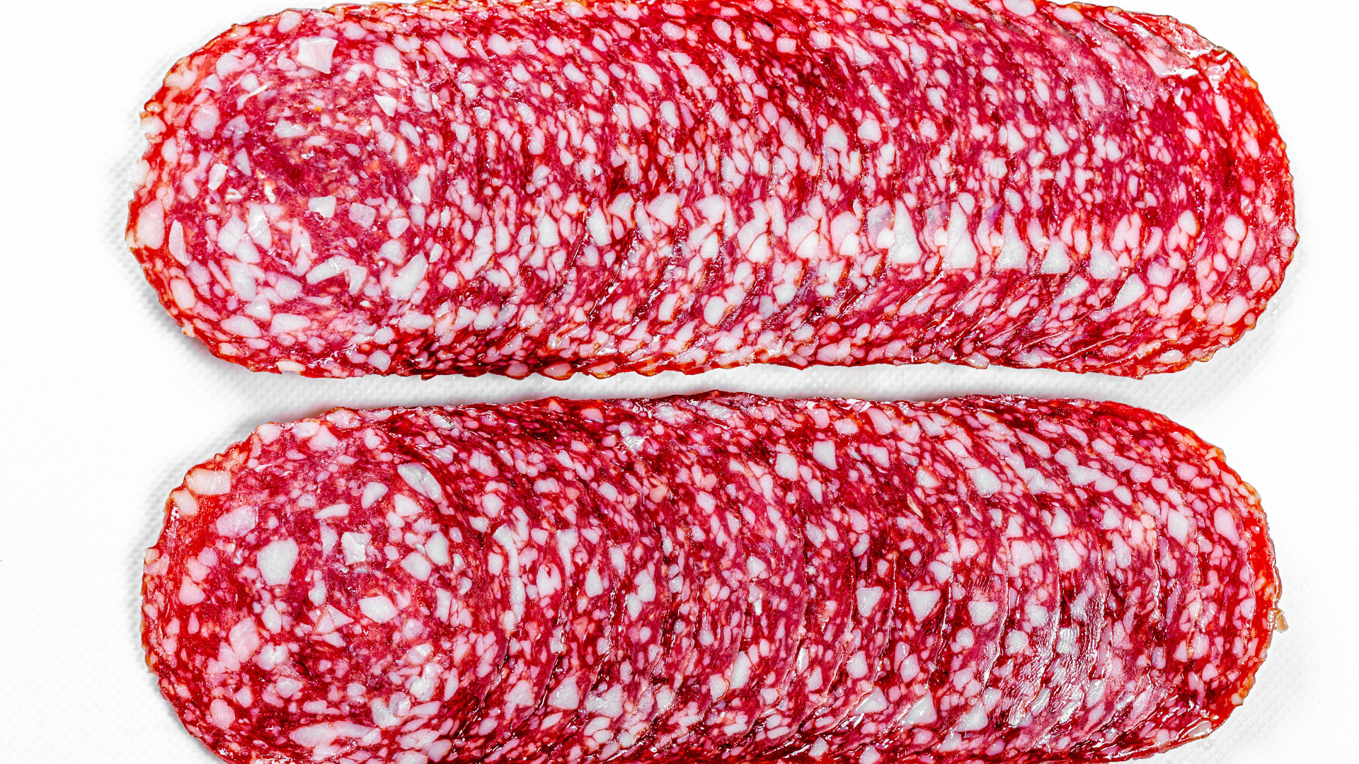 Колбаса салями нарезанная тонкими кусочками на белом фоне