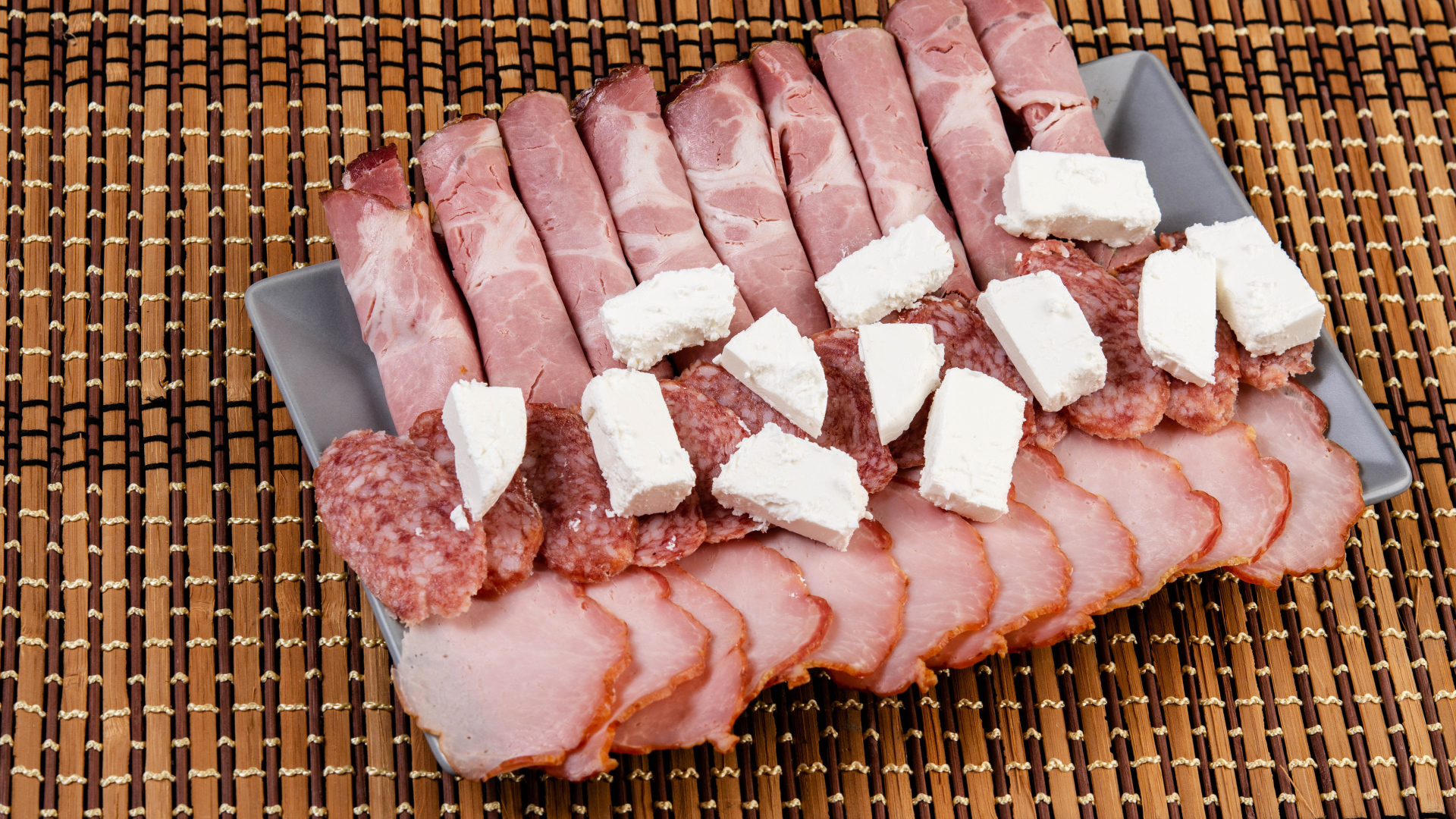 Колбаса и ветчина на тарелке с кусочками сыра фета