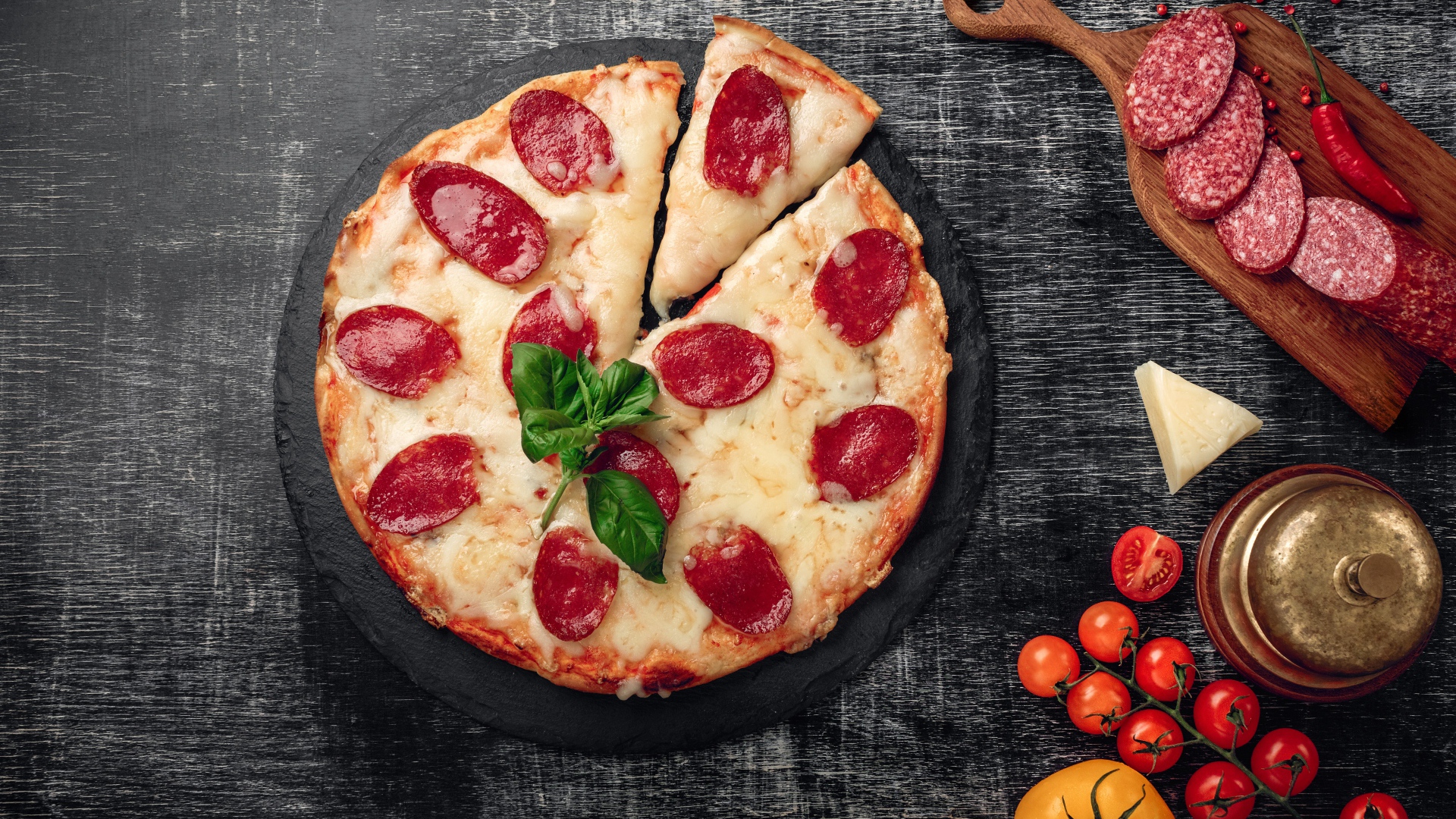 Pizza with cheese and salami on the table with tomatoes and sausage