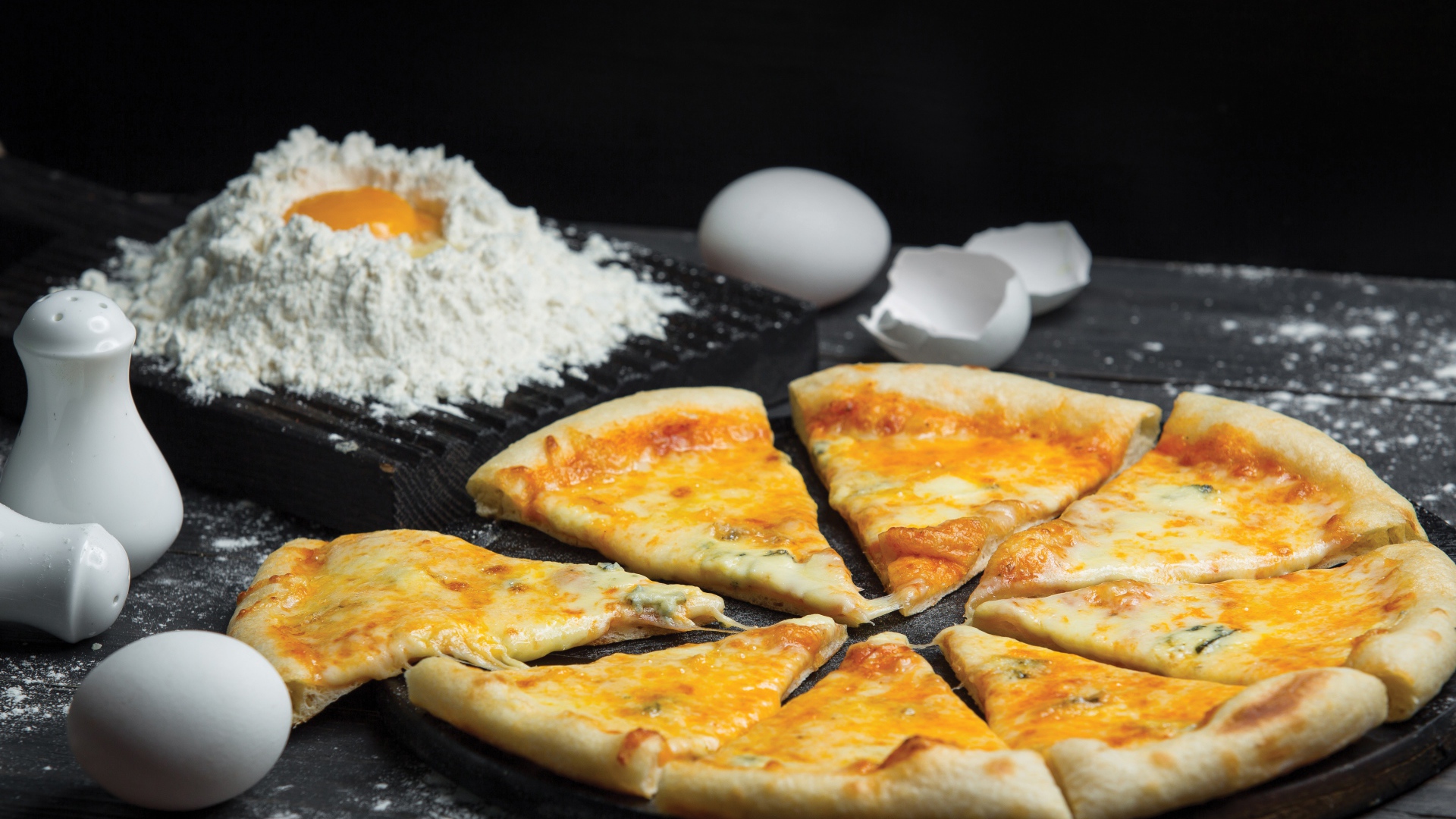 Пицца с сыром нарезана кусочками на столе с мукой и яйцами