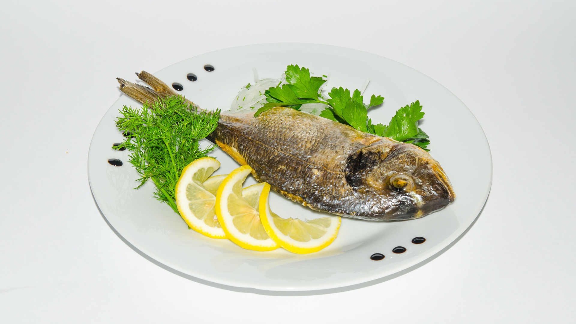 Запеченная рыба на тарелке с лимоном и зеленью 
