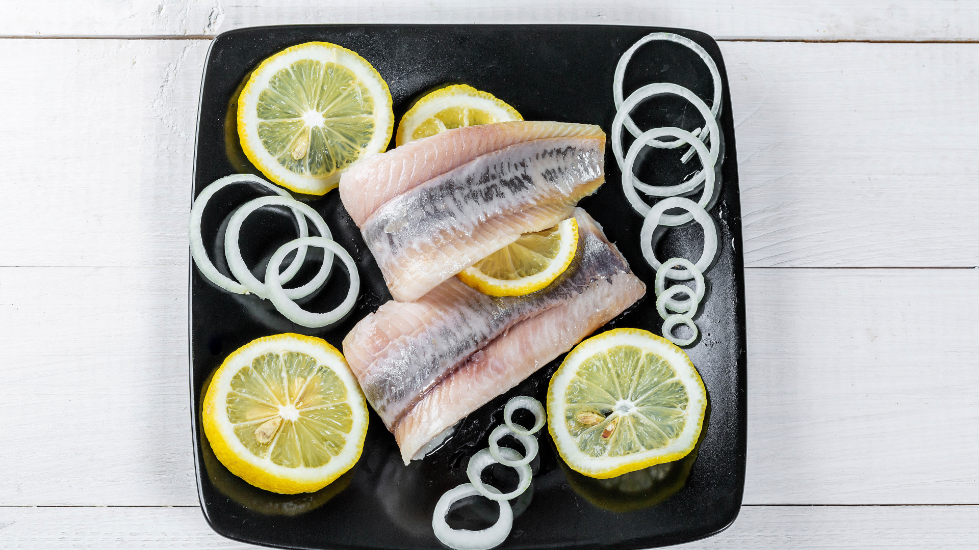 Филе сельди на черной тарелке с луком и лимоном