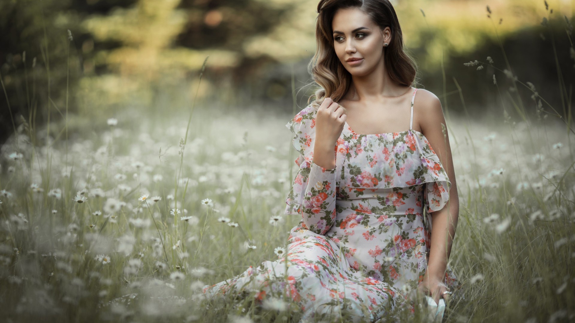 Красивая девушка в сарафане сидит на поляне с ромашками 