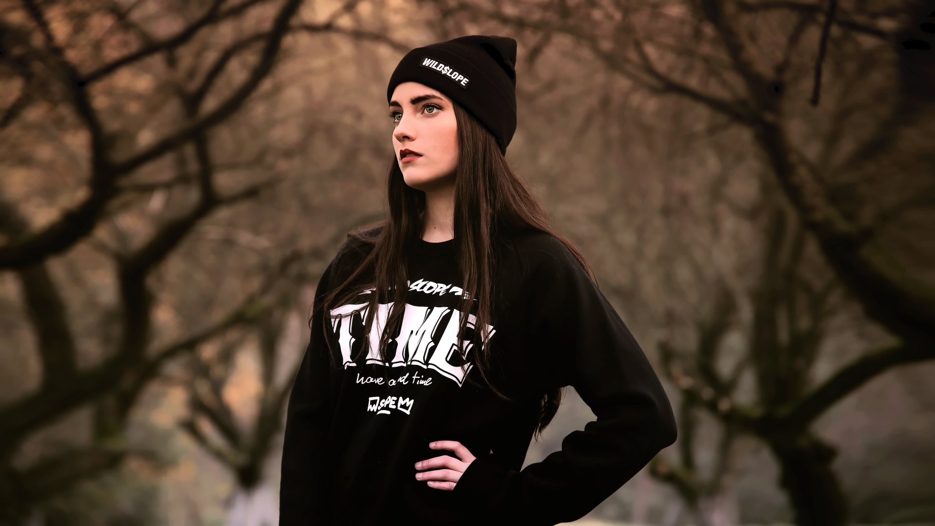 Красивая девушка в черной шапке у деревьев 