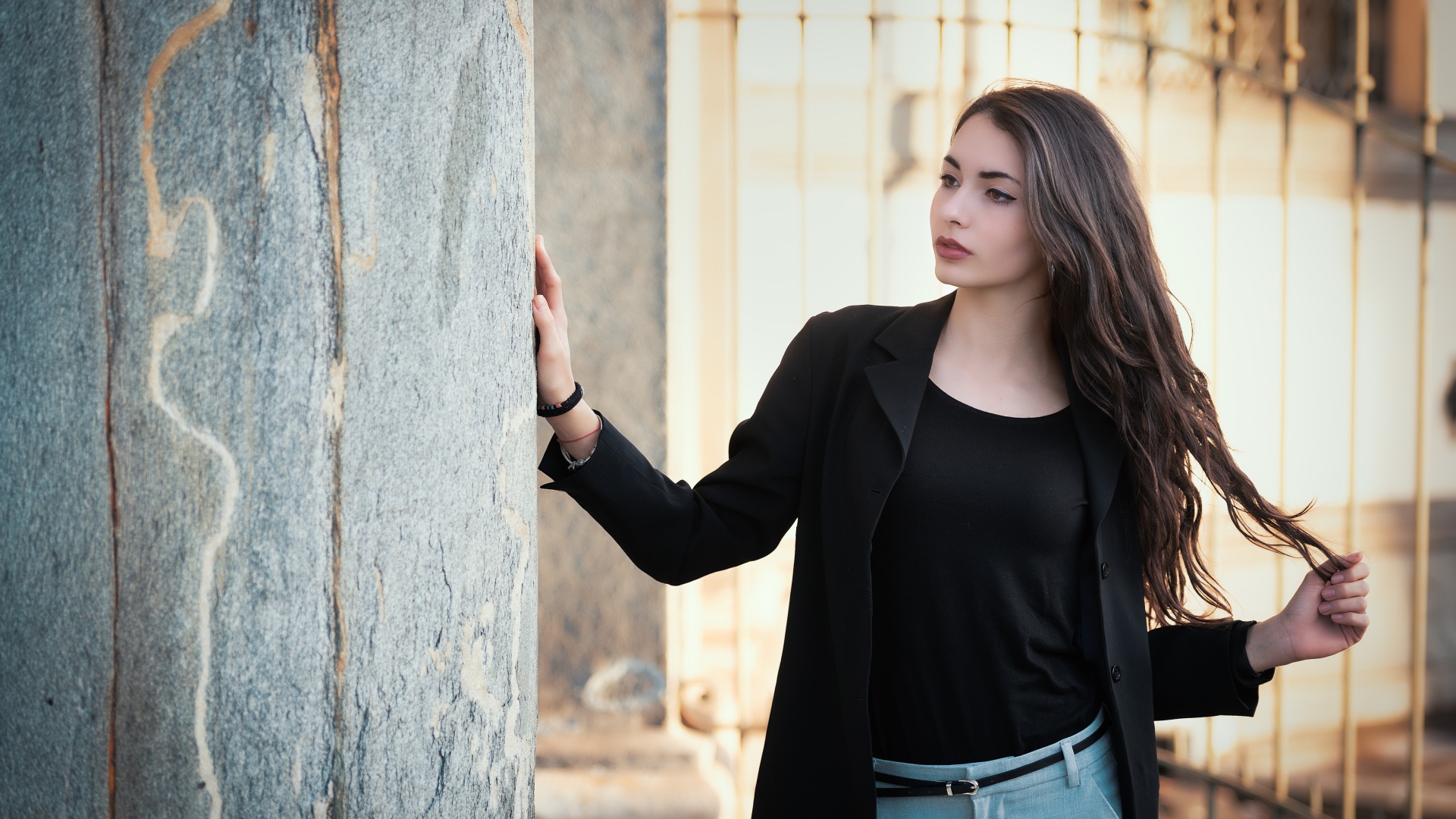 Красивая девушка в черном пиджаке стоит у стены