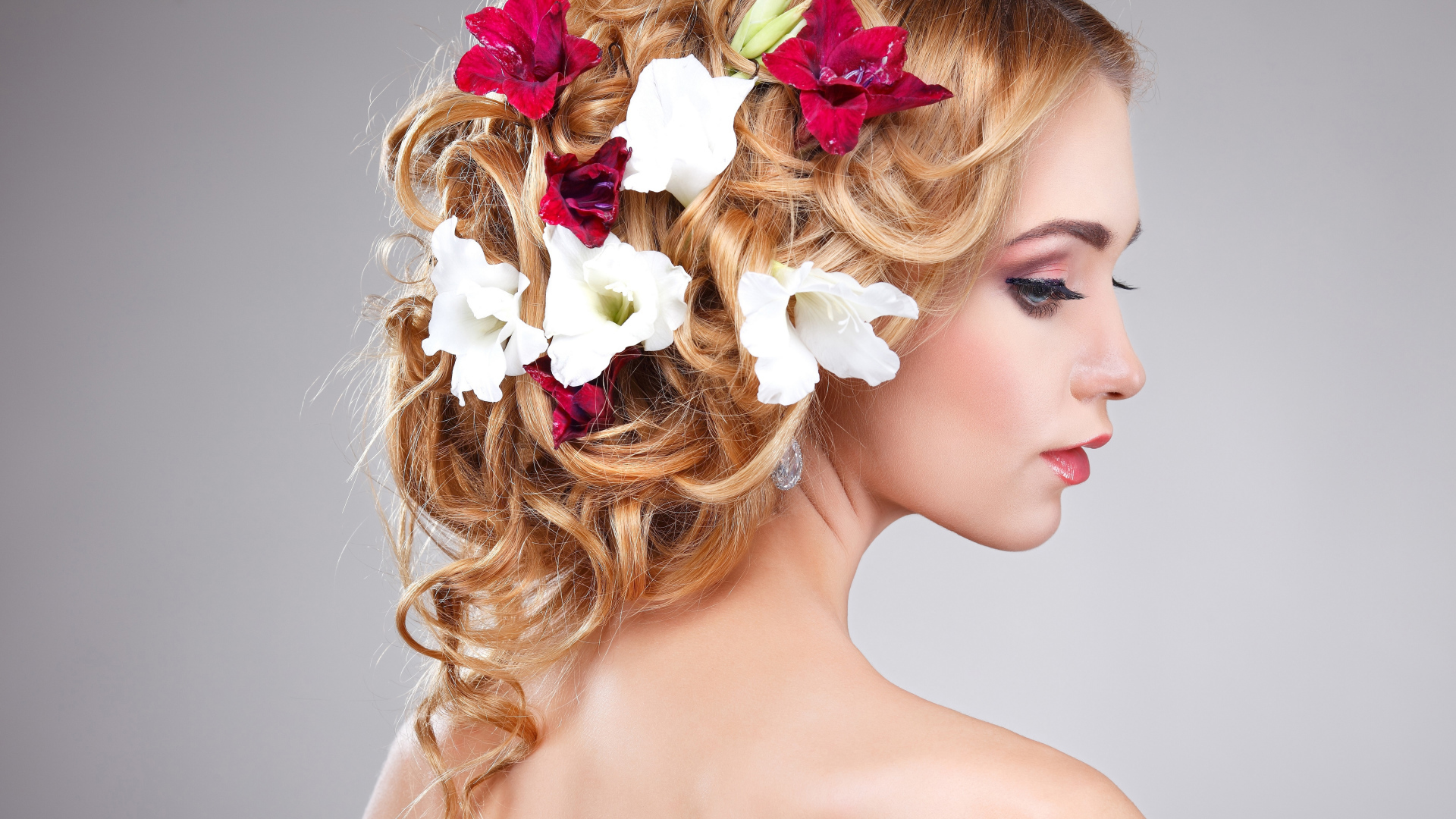 Красивая девушка с цветами петунии в волосах на сером фоне