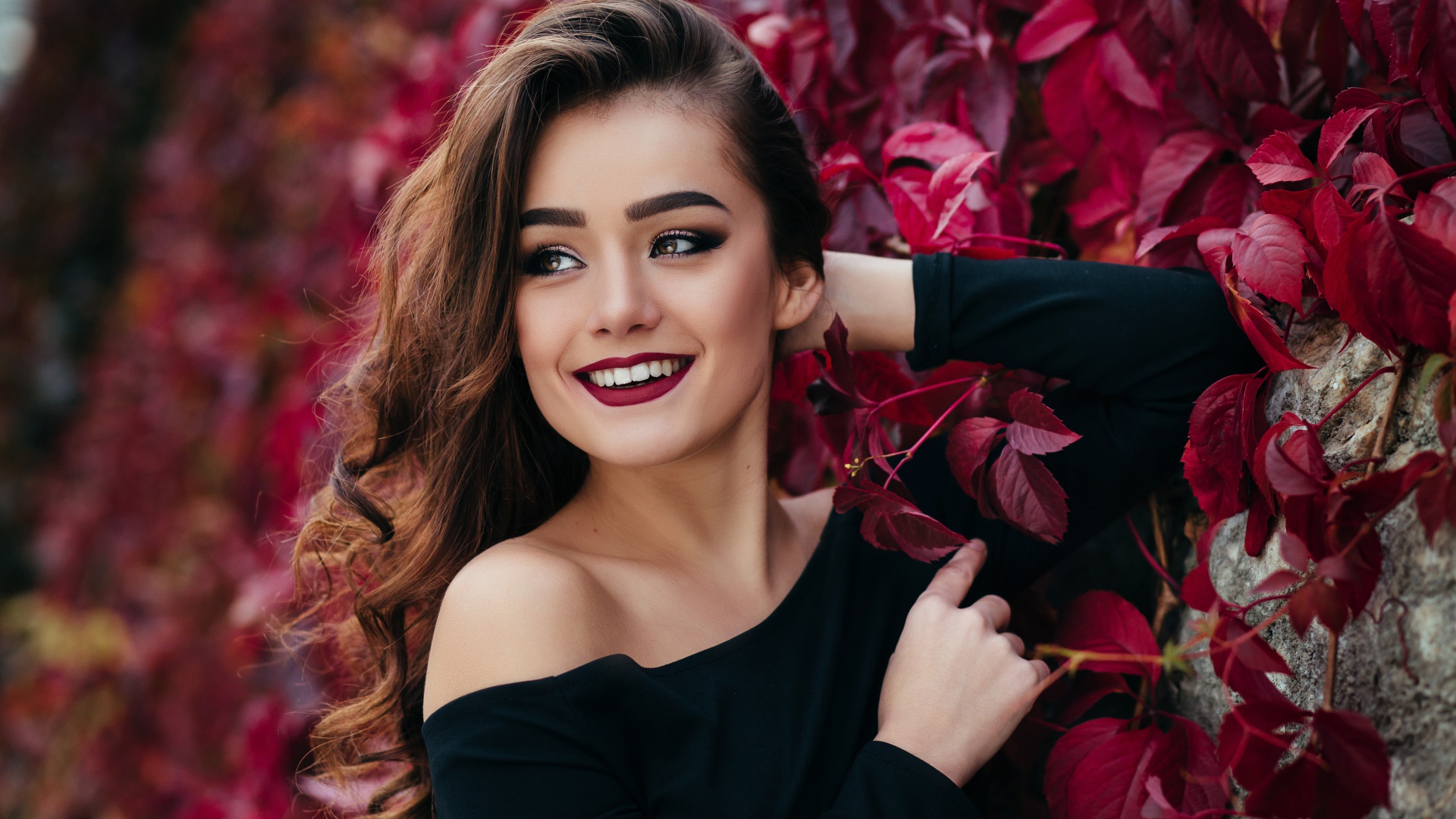 Красивая улыбающаяся длинноволосая девушка у стены с декоративным виноградом