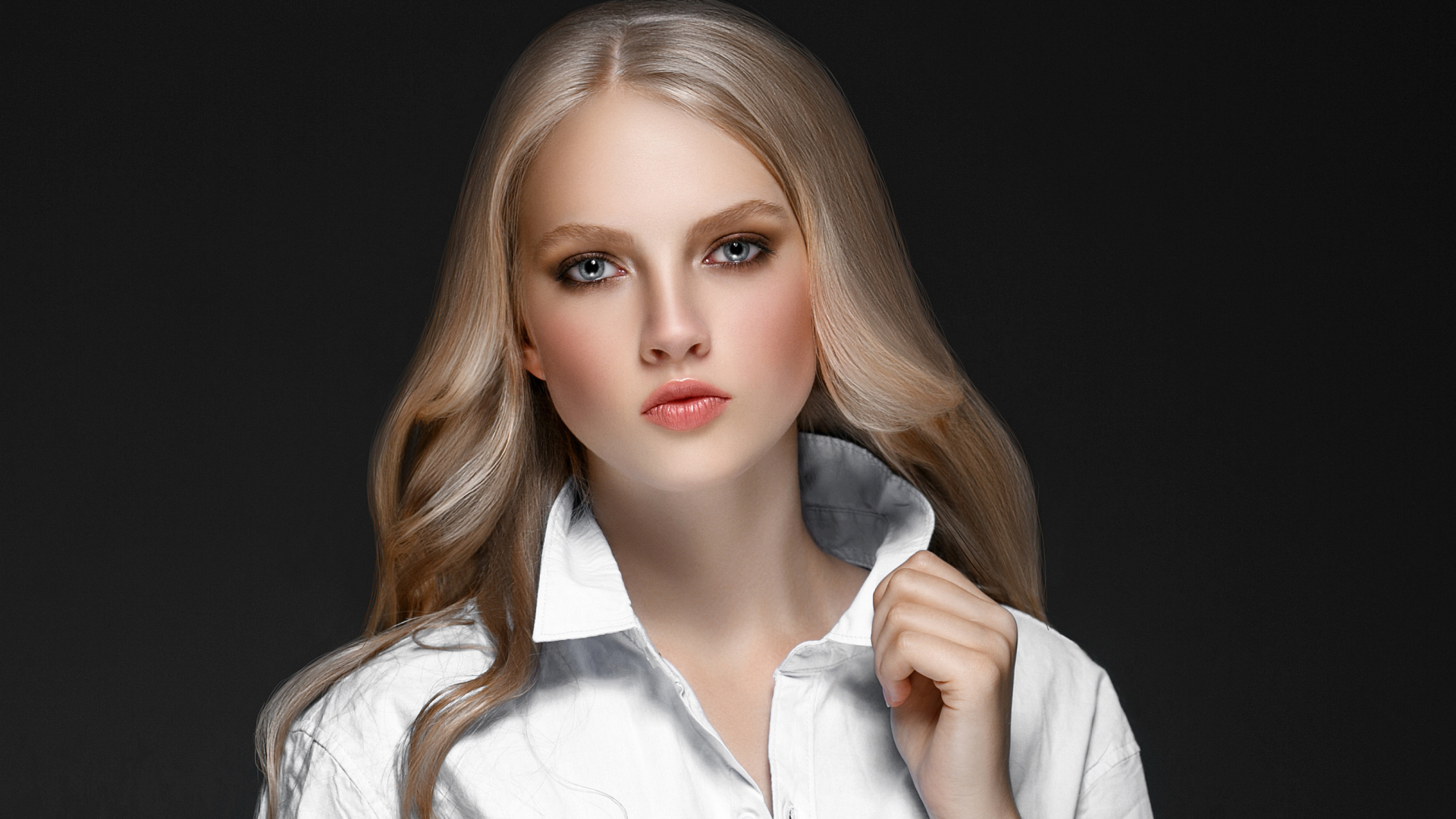 Красивая стильная голубоглазая блондинка в белой рубашке на сером фоне