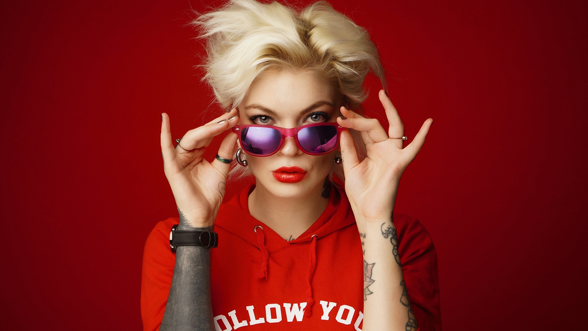 Яркая блондинка с татуировками на руках на красном фоне